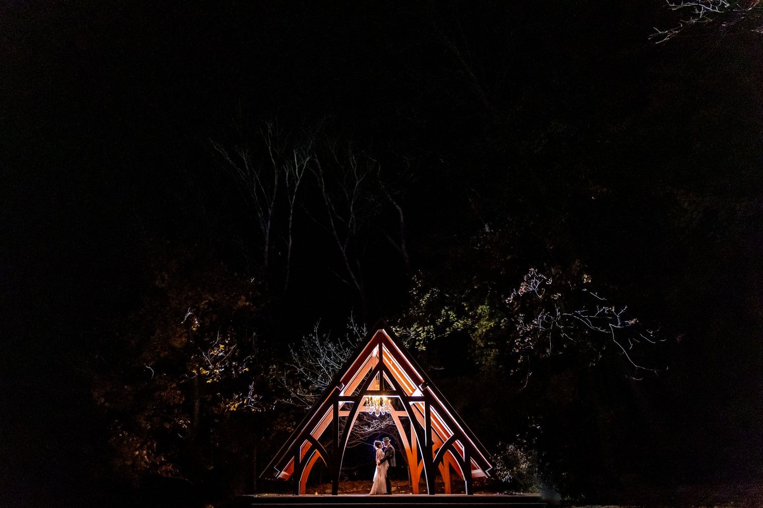 Silhouetted campfire scene with teepee-style structure against dark night sky.