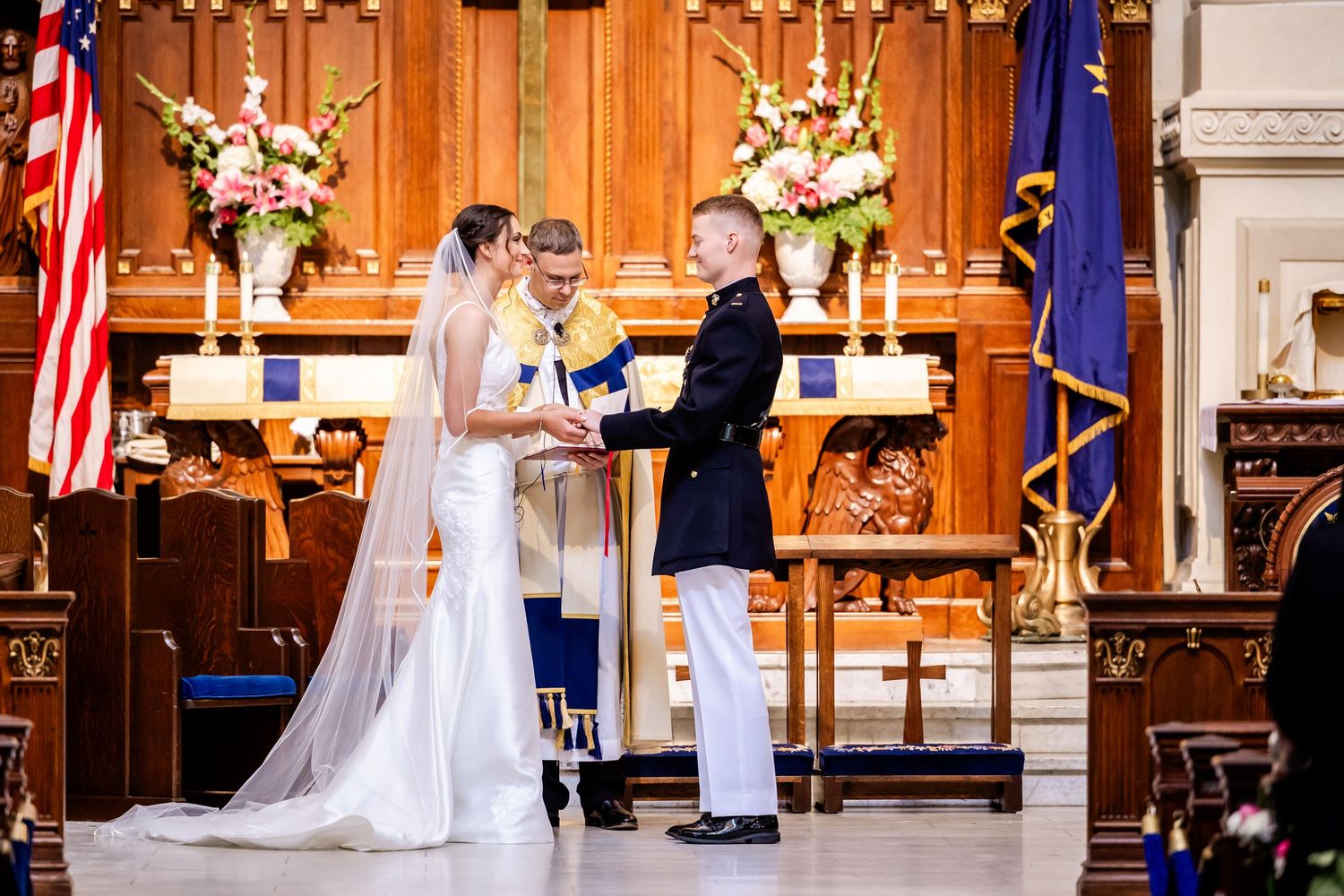 Military wedding ceremony taking place in a traditional church with floral arrangements and American flag.