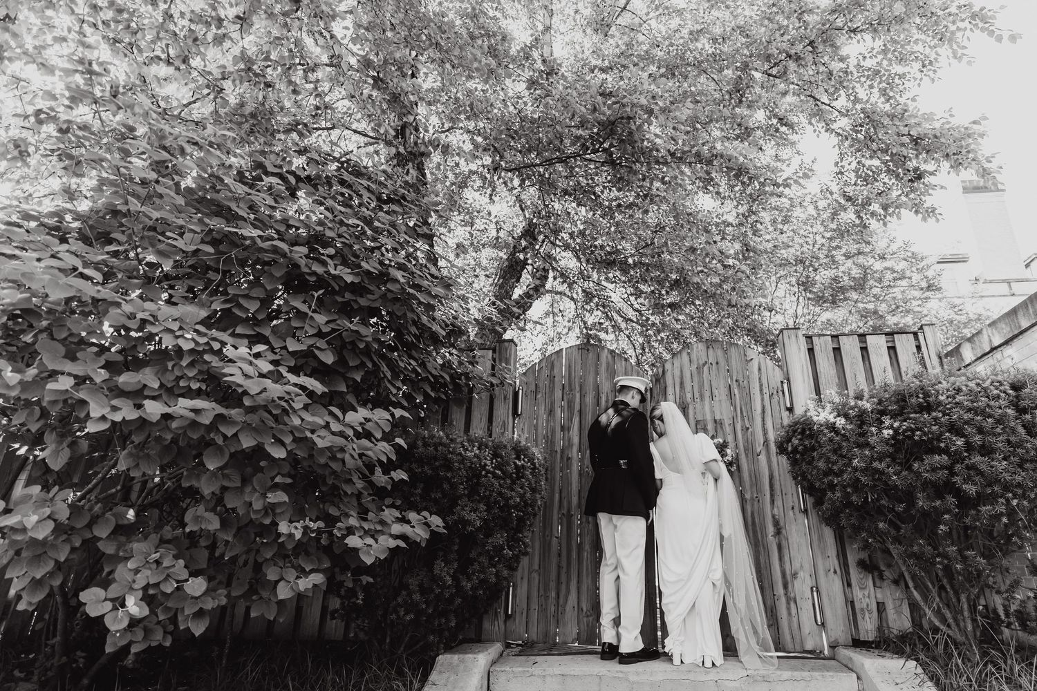Wedding party poses among trees and greenery in outdoor garden setting.