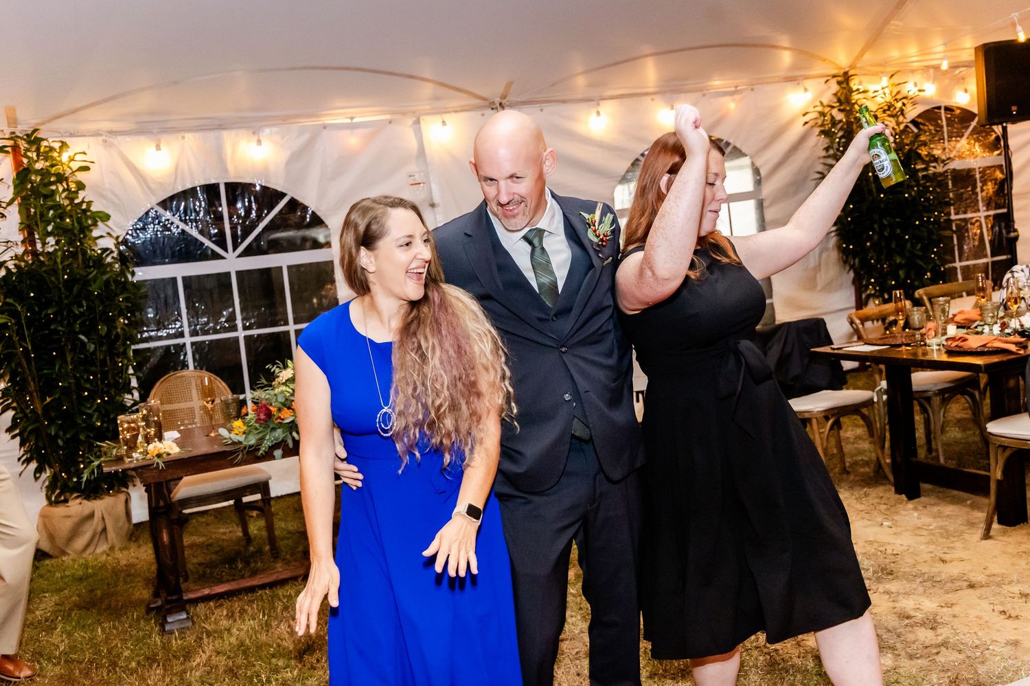 Wedding guests dancing and celebrating under tent lighting at reception.