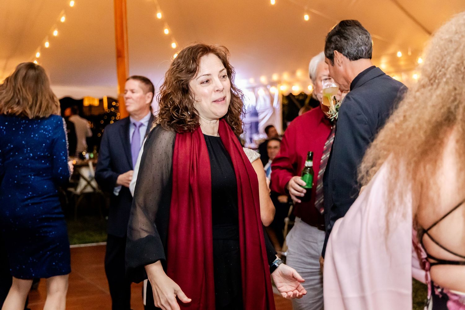 Reception party with guests dancing under warm tent lighting.