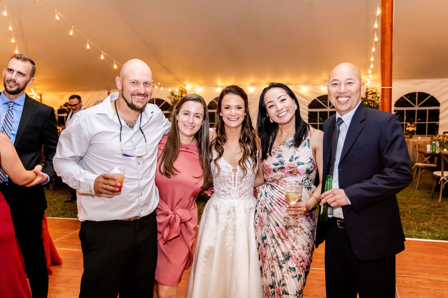 Wedding reception guests mingling and celebrating under a tent with string lights.
