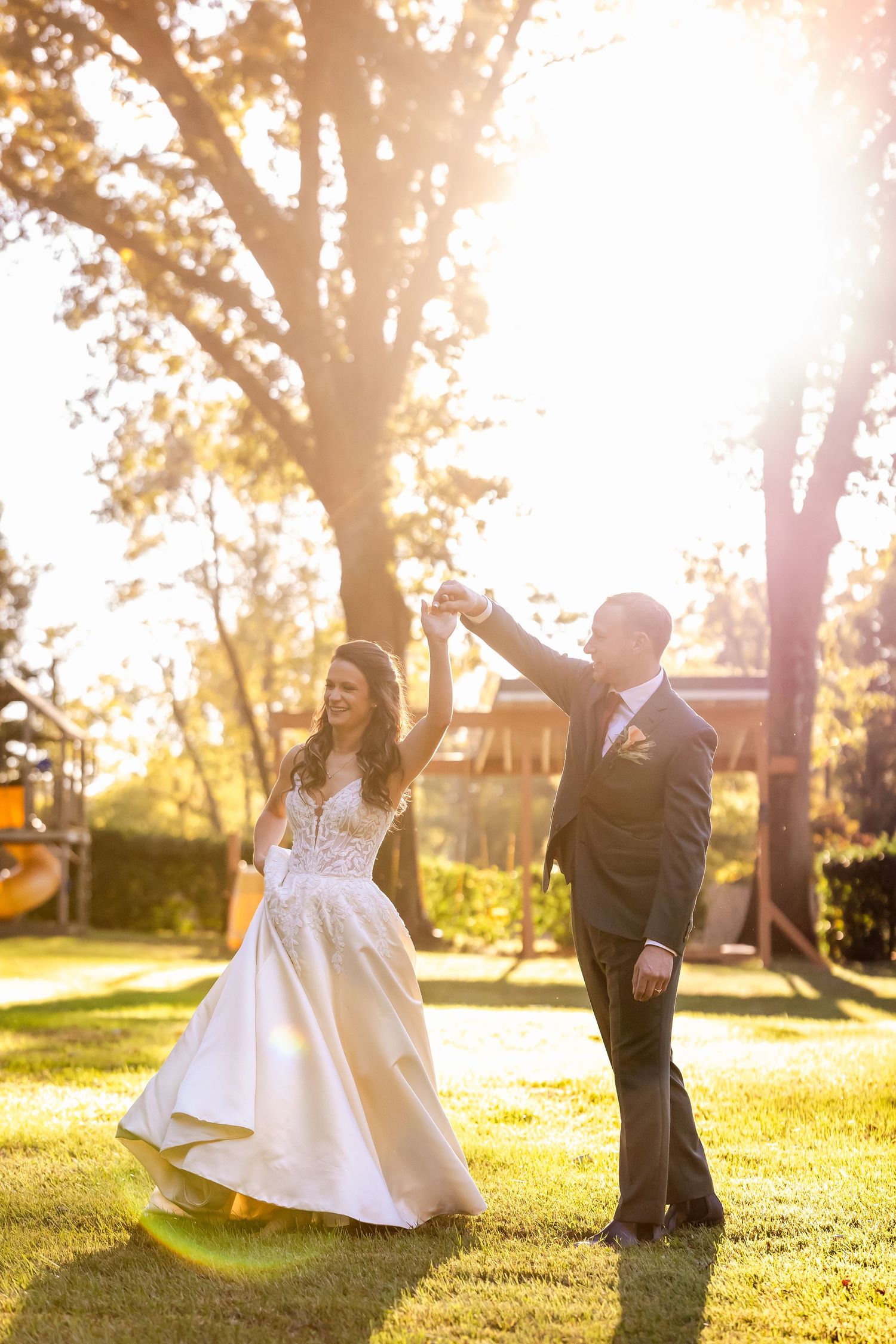 A couple dances playfully in a sunlit park during golden hour with trees in the background.