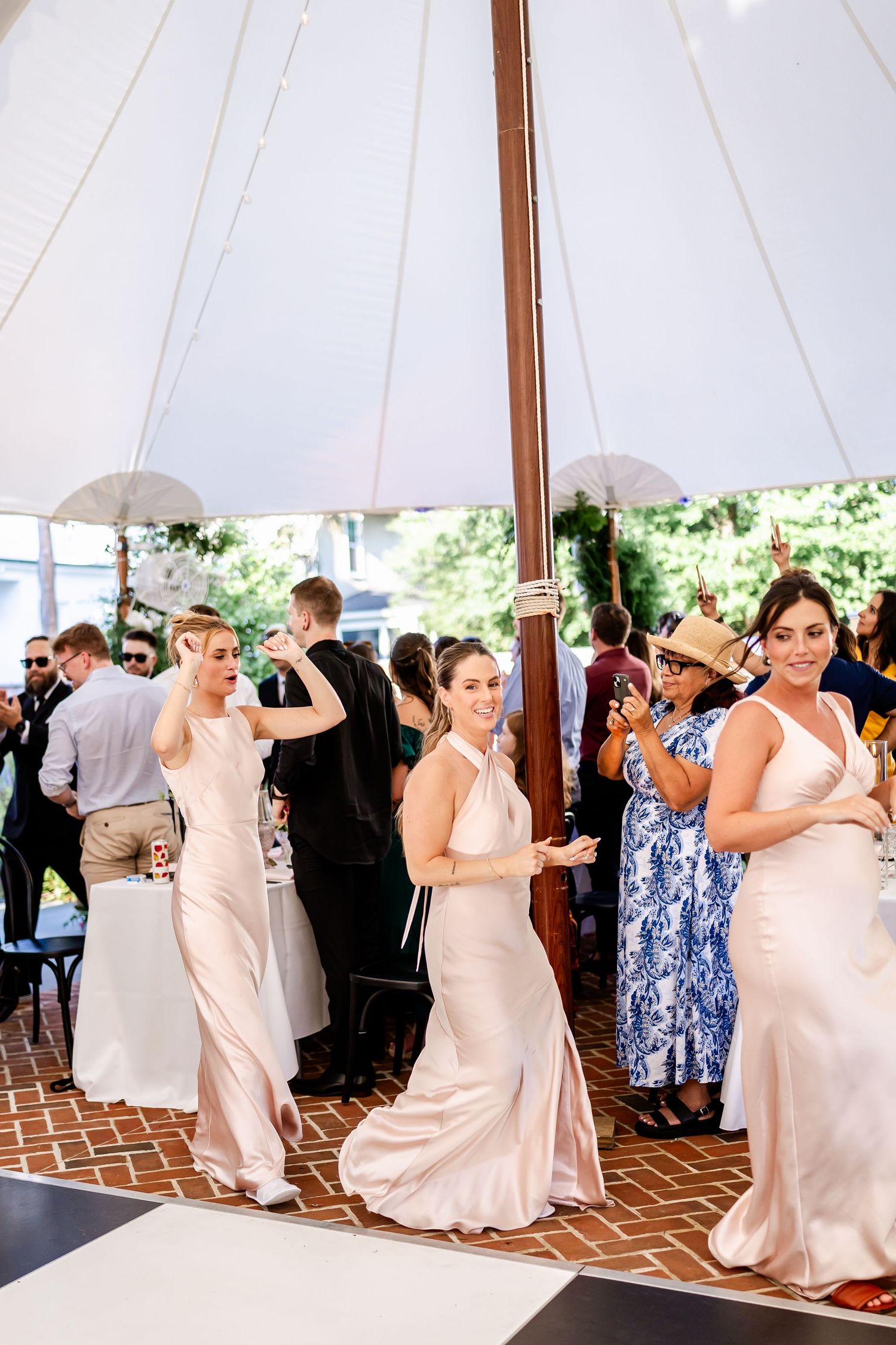 Wedding party dances together under an elegant white tent during a reception celebration.