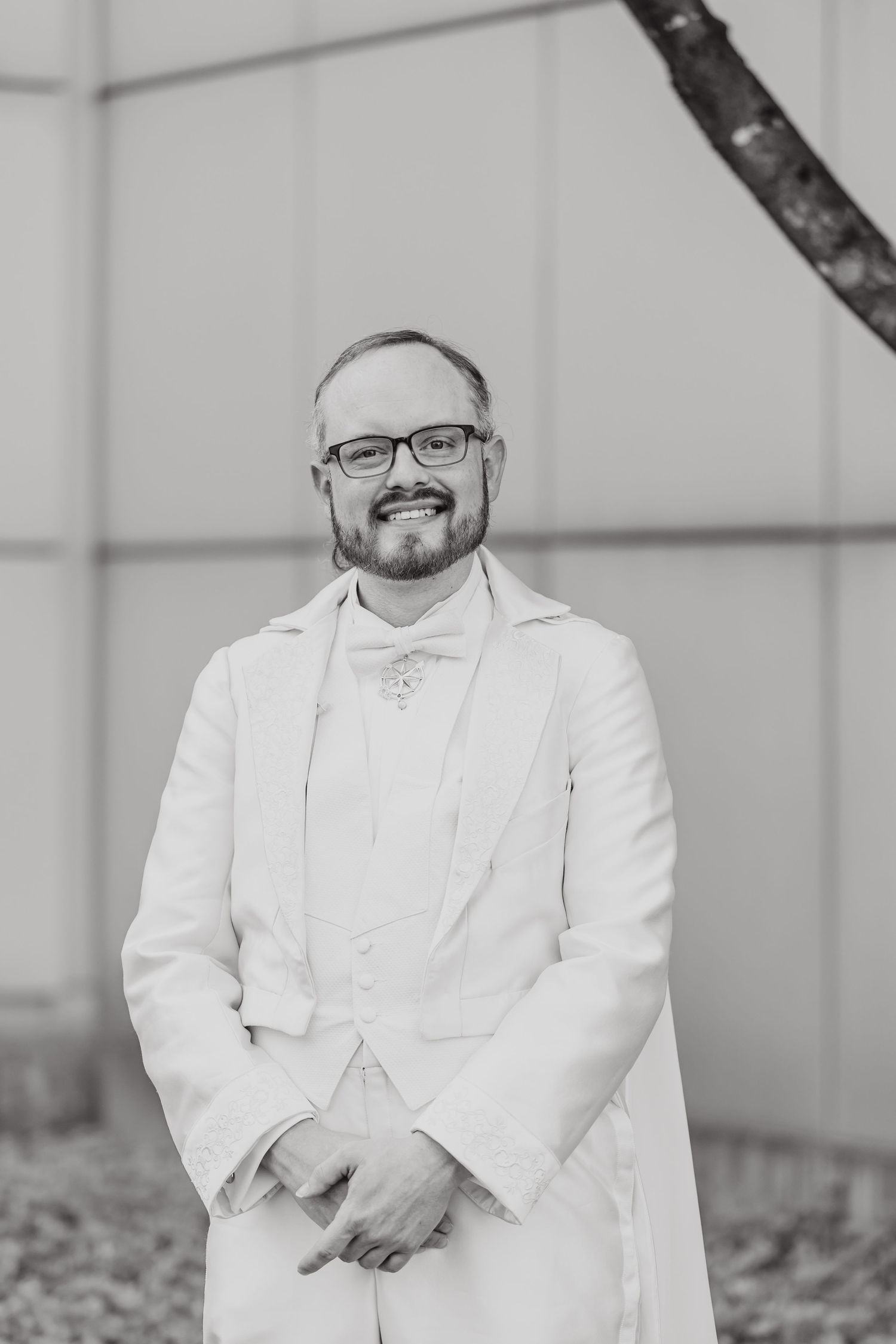 Classic black and white portrait of groom in white suit and glasses.