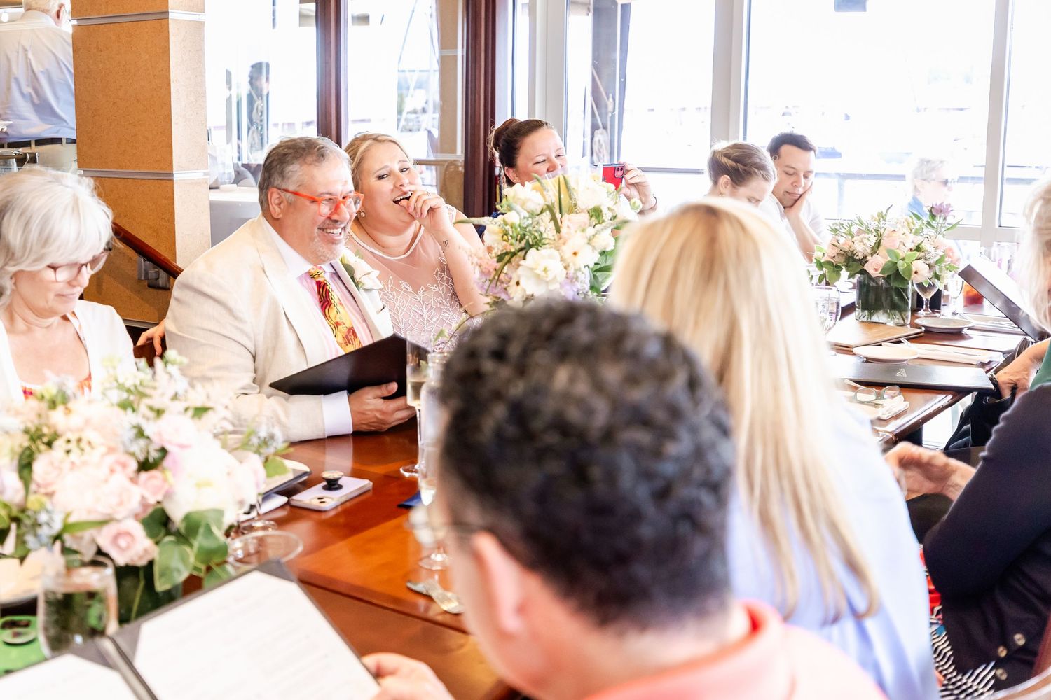 Guests enjoy a celebratory meal at a long dining table decorated with white floral centerpieces.