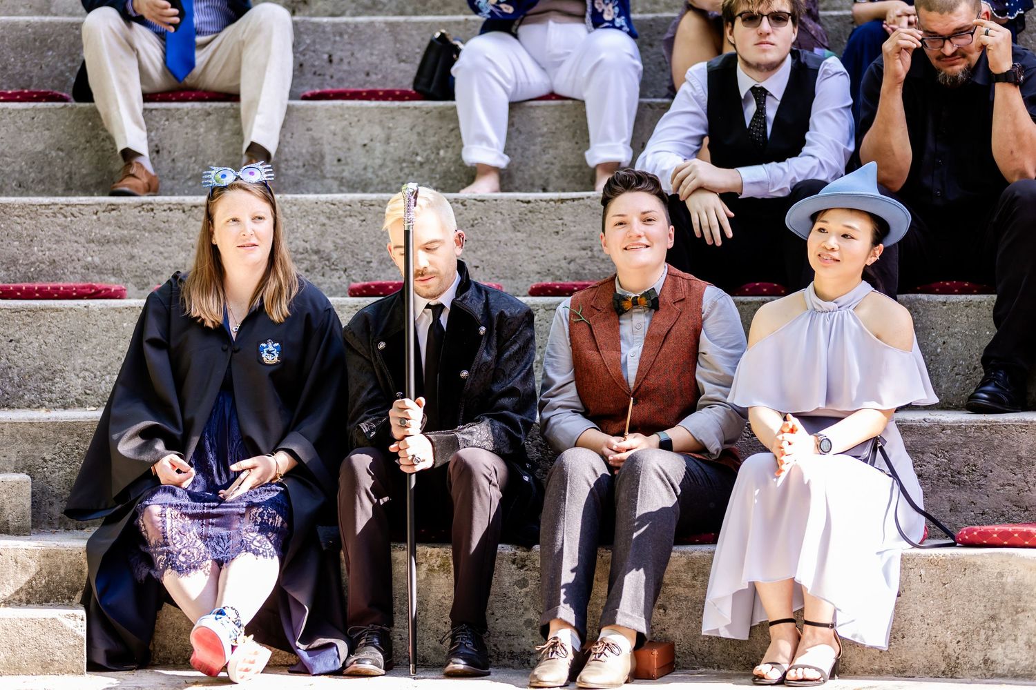 Wedding guests seated on stone steps in formal attire.