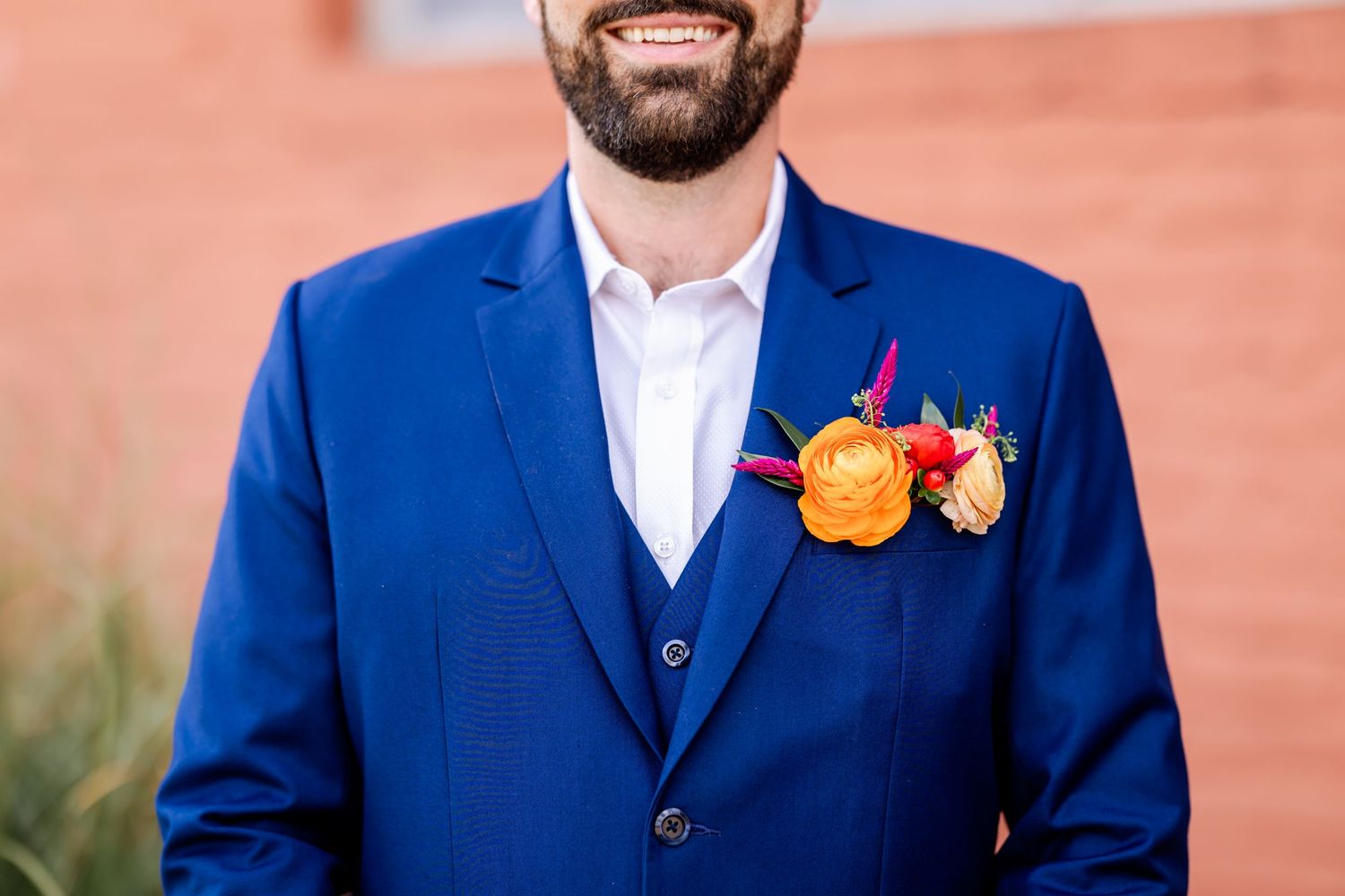 Close up of blue suit jacket with orange and pink floral boutonniere.