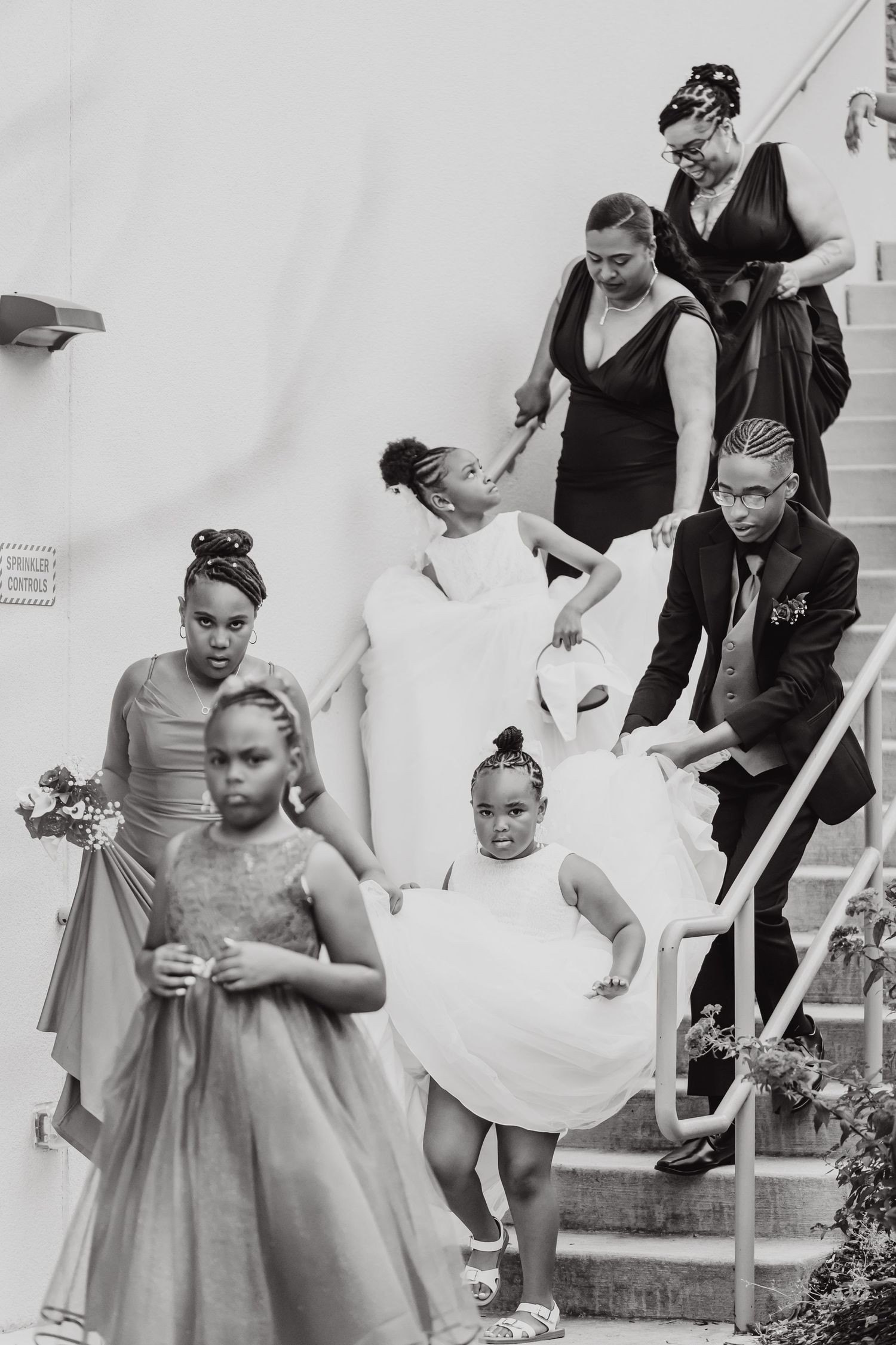 Wedding party members in formal attire walking down white stairs.