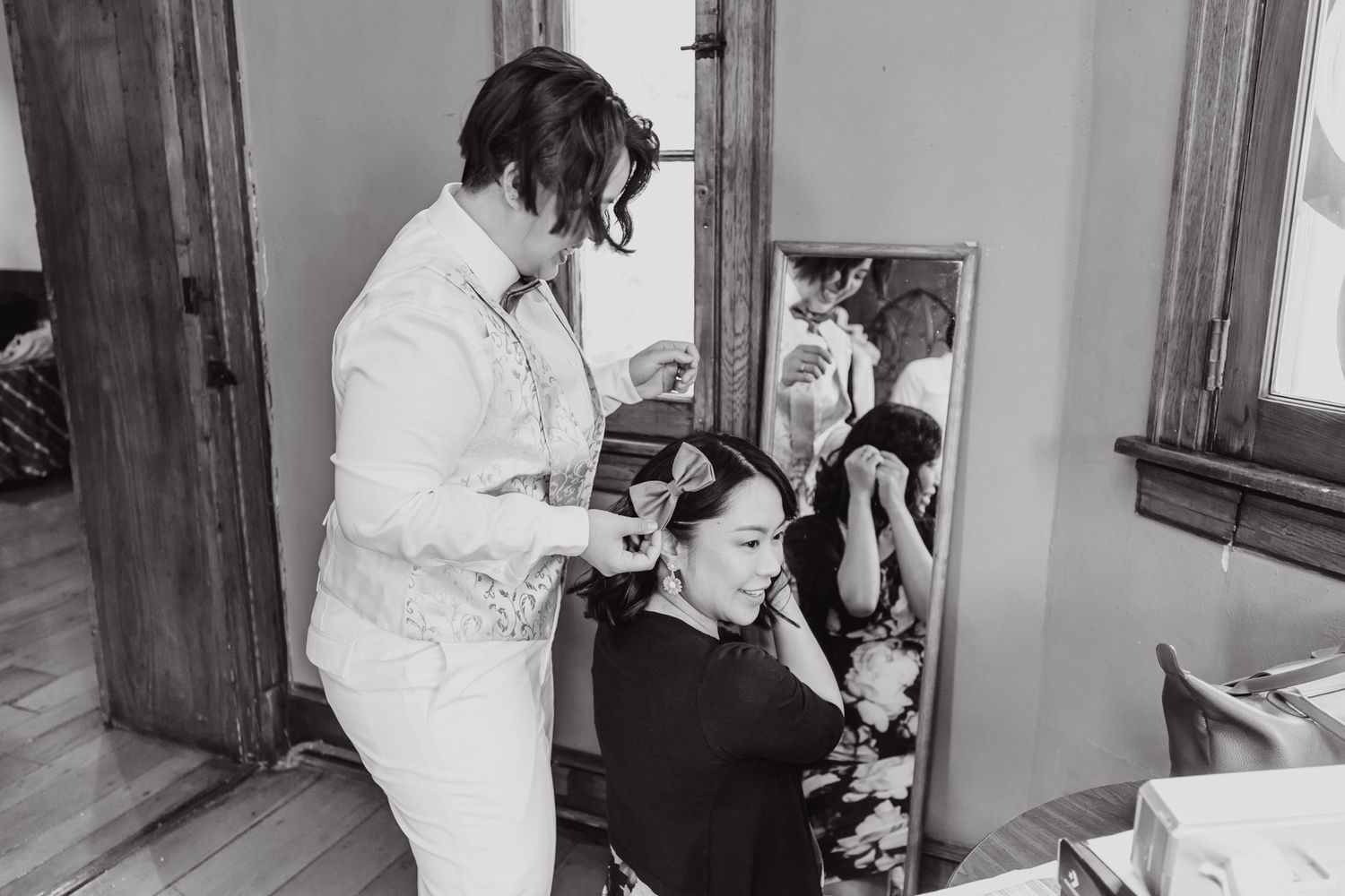 Two people prepare for a formal event in a sunlit dressing room.