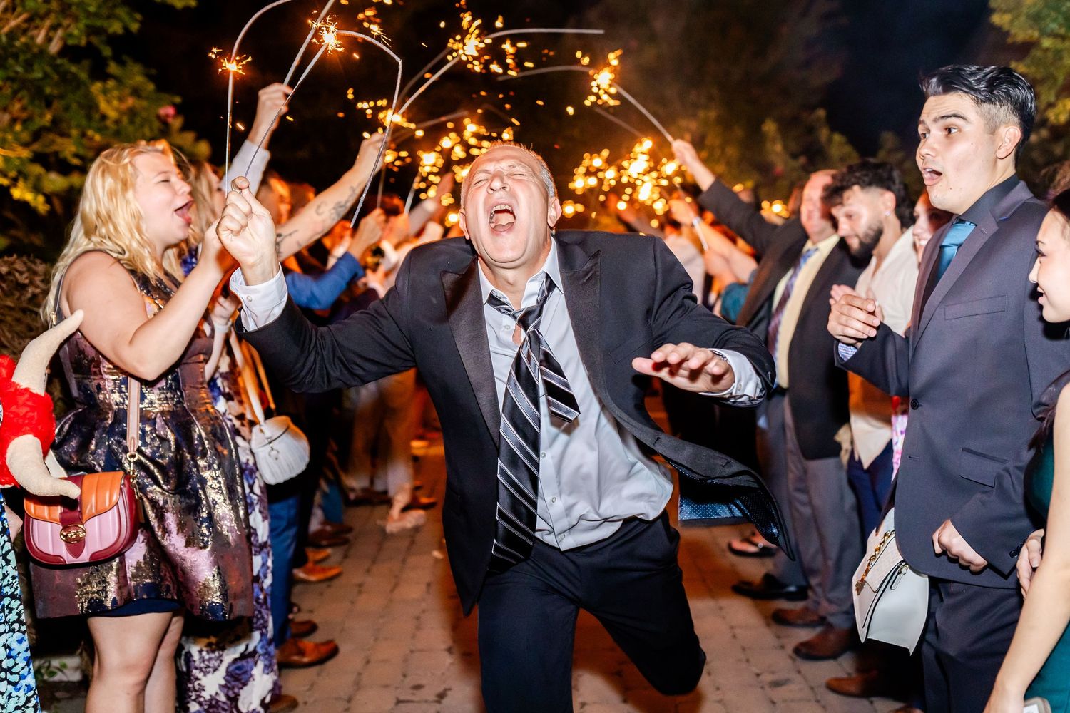Wedding party guests celebrate joyfully with sparklers during an outdoor nighttime celebration.