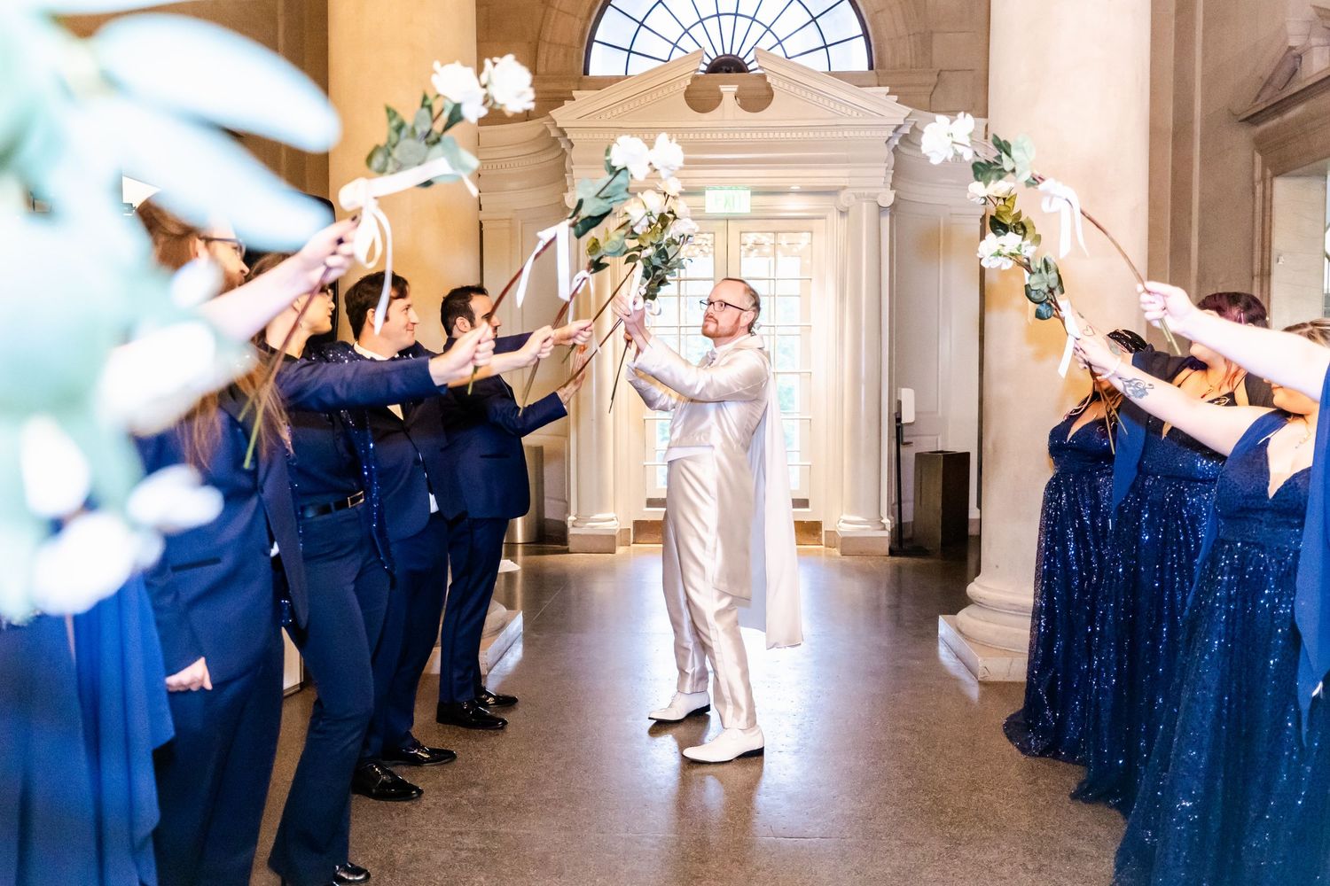 Wedding party creates sparkler tunnel exit inside ornate venue hallway.