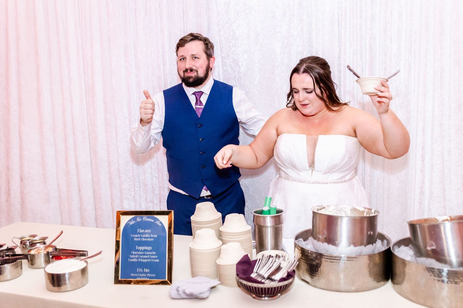 Wedding couple making animated gestures while serving food at their reception buffet.