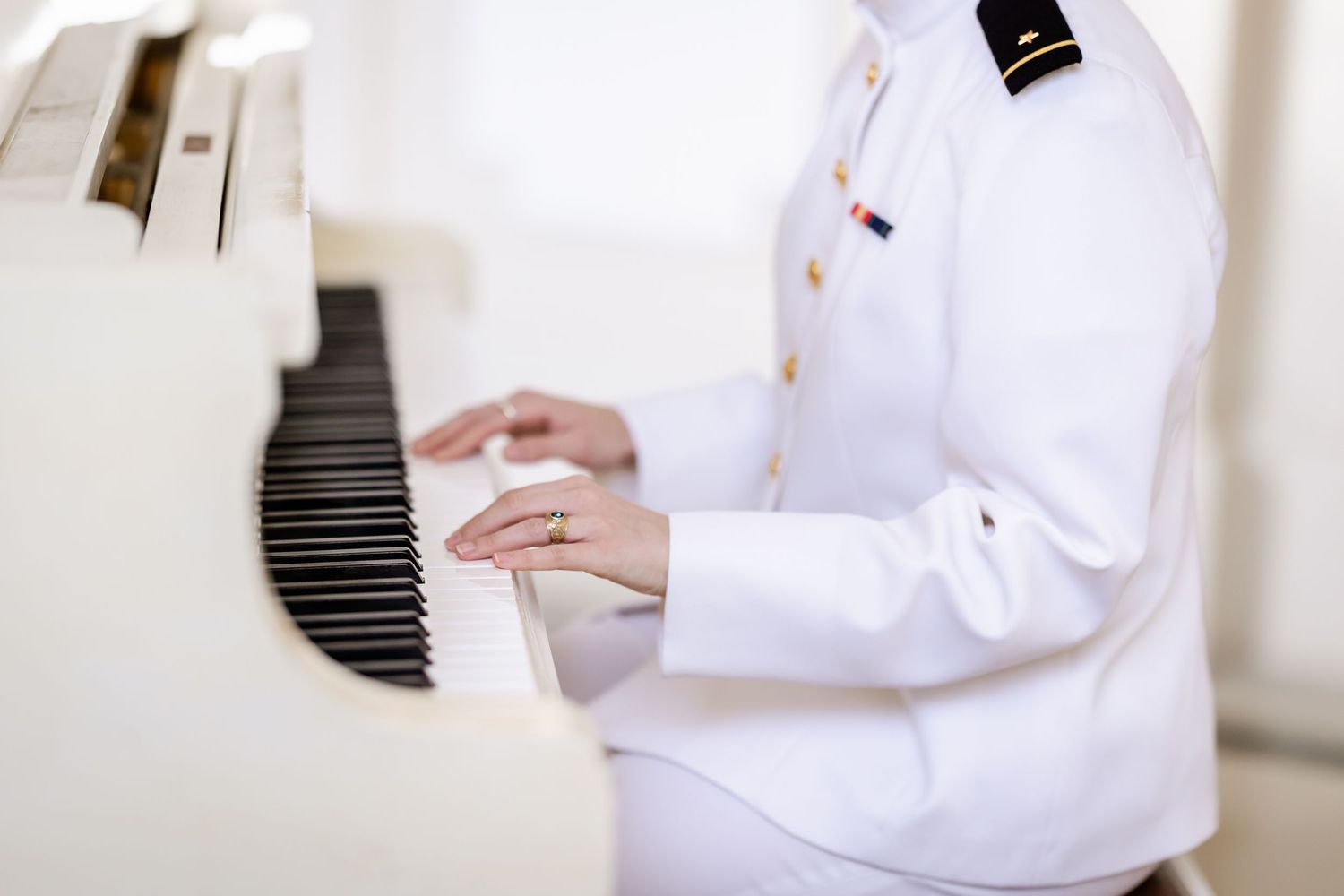 Someone wearing a crisp white chef's coat plays a white piano with delicate hands.