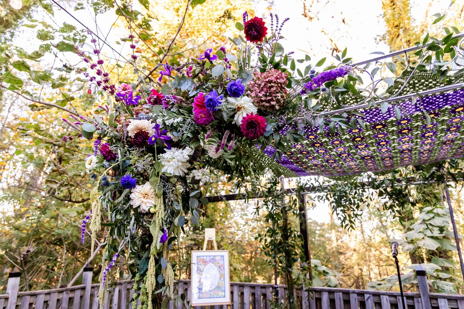 Stunning floral arch with purple and pink blooms decorating an outdoor wedding ceremony space.