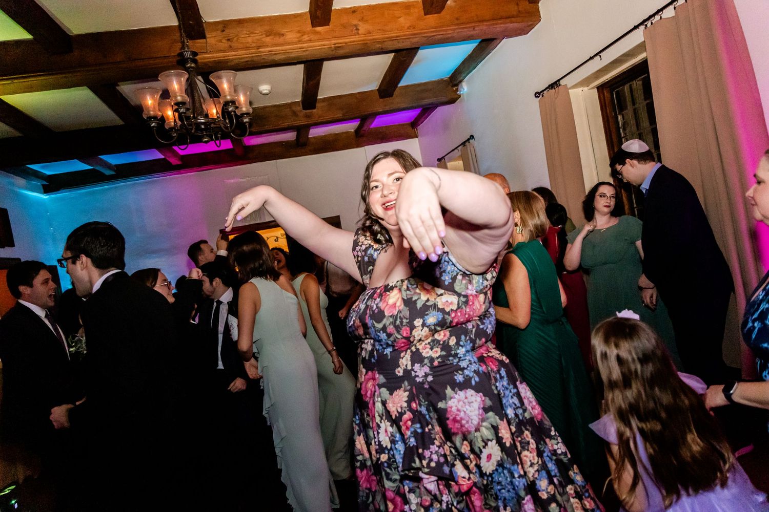 Joyful wedding guest dancing enthusiastically under colorful lights at reception party.