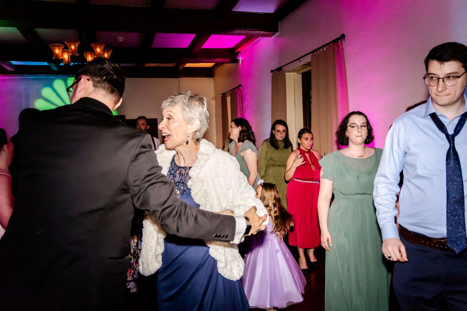 Wedding reception dance floor filled with guests enjoying colorful lighting and festivities.