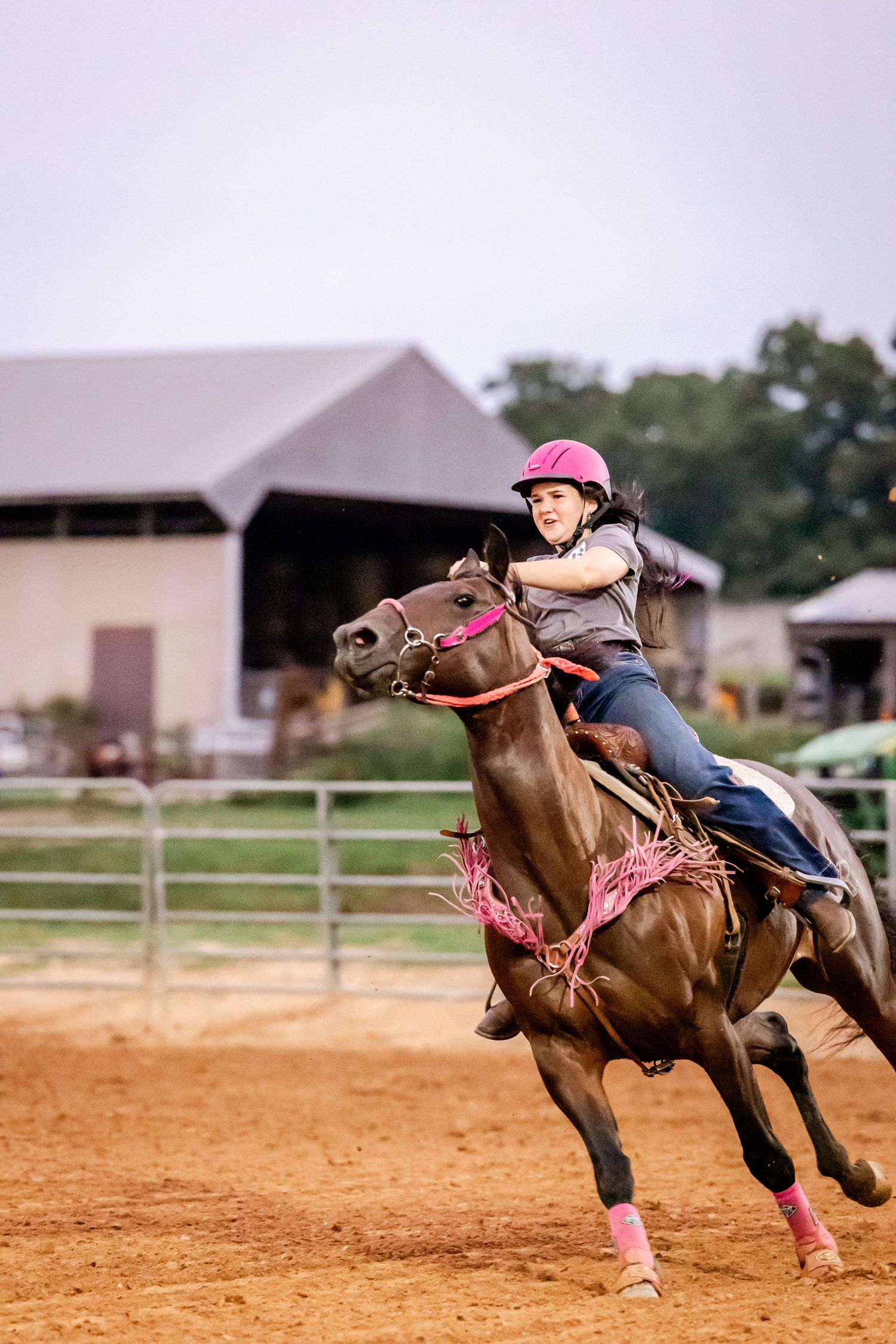 Competitive barrel racer in pink helmet rounds corner at full gallop.