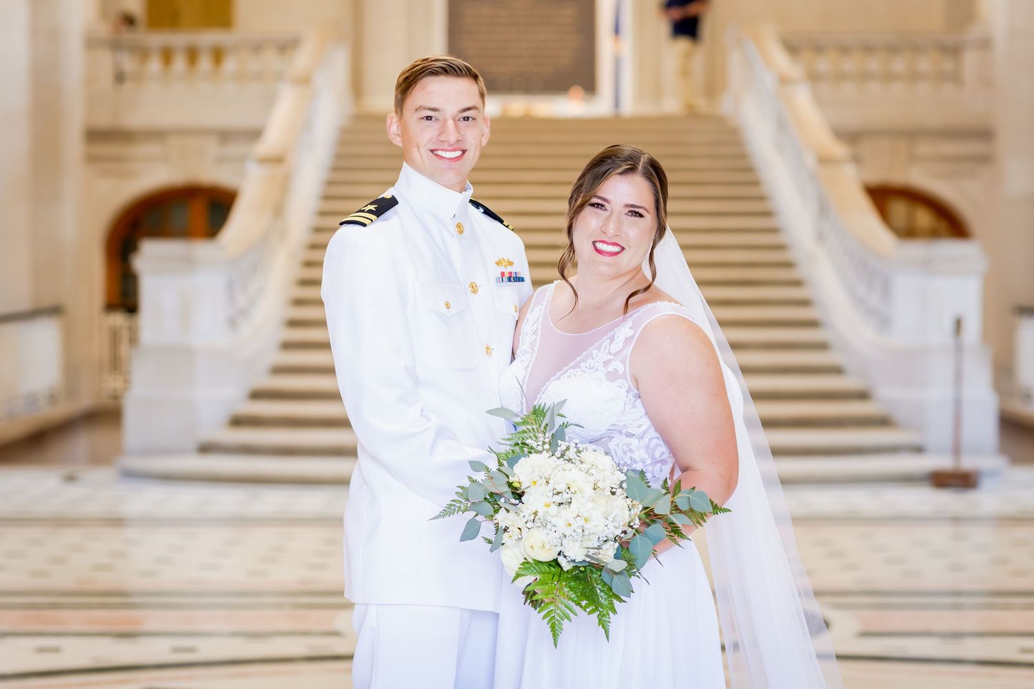 Bride and groom share an intimate moment on an ornate marble staircase in a grand building interior.