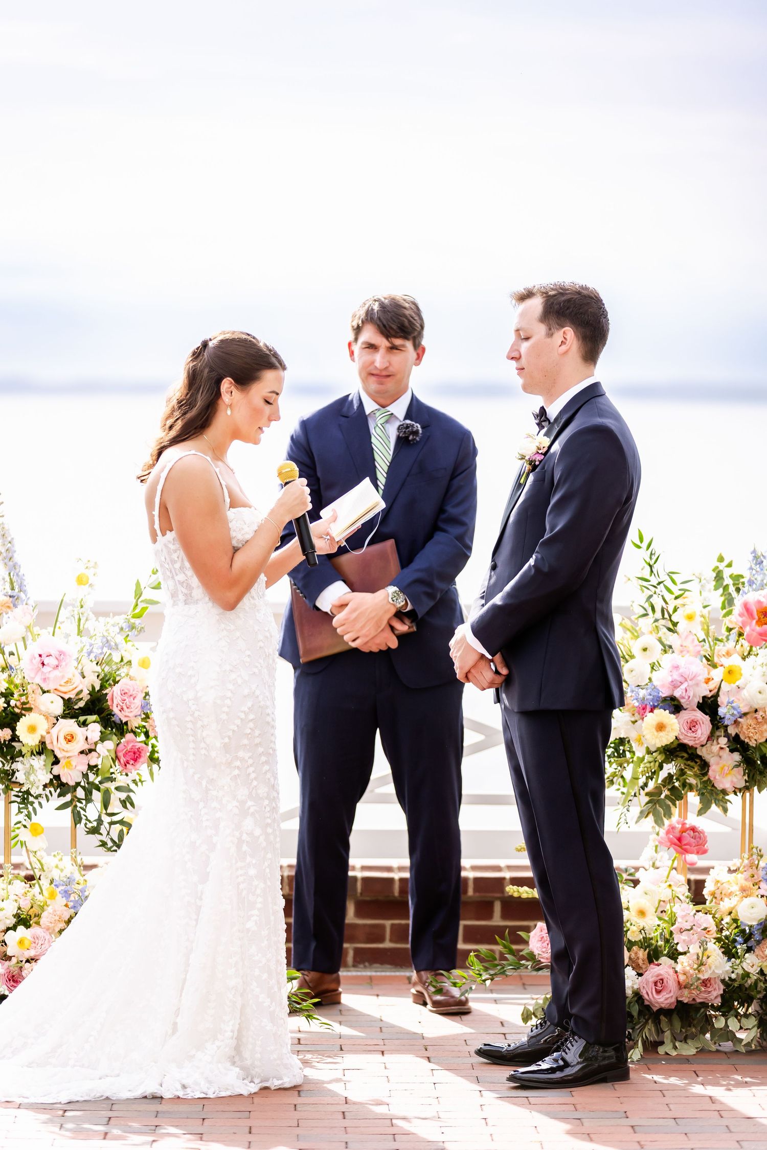 Outdoor wedding ceremony with floral arrangements and waterfront view showing emotional exchange of vows.