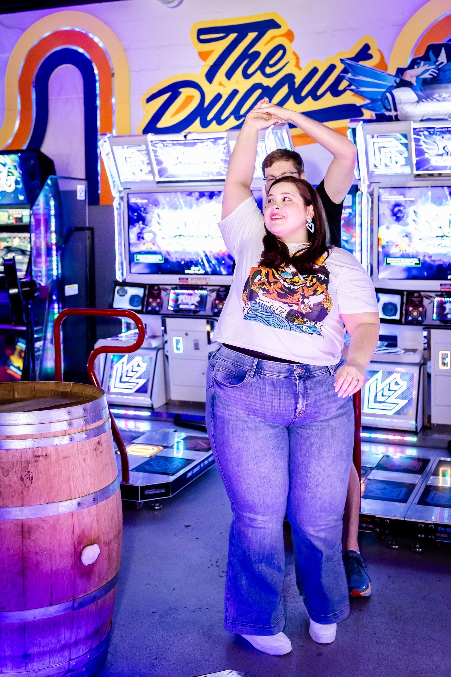 Retro arcade interior decorated with purple lighting features neon signs and a large wooden barrel.