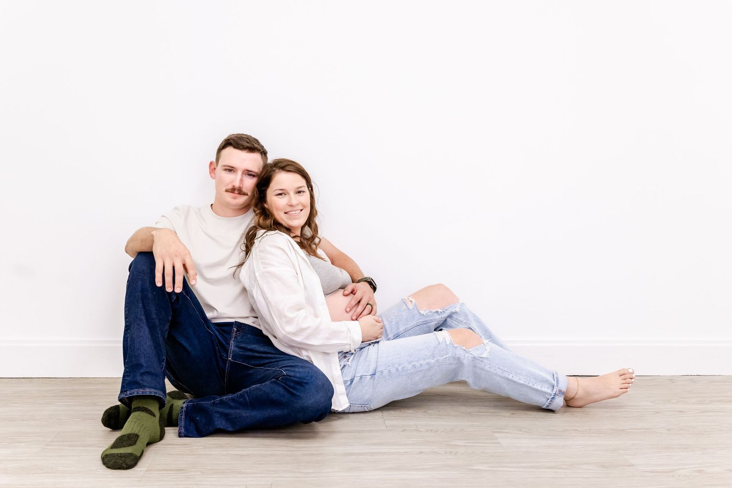 Relaxed couple sitting on floor against white wall in coordinated casual outfits.