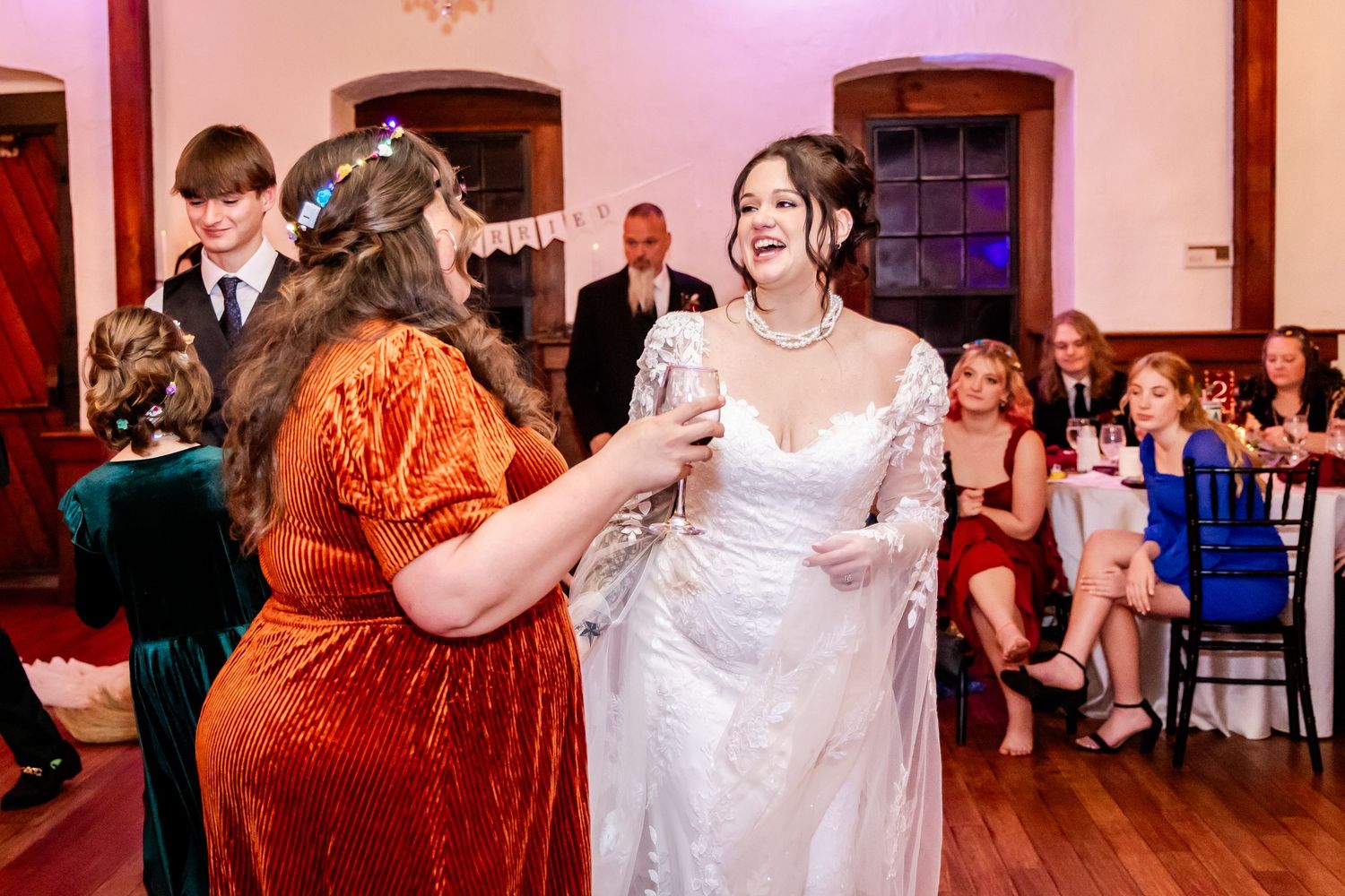 Wedding reception guests dancing and celebrating in a warmly lit ballroom with pink uplighting.
