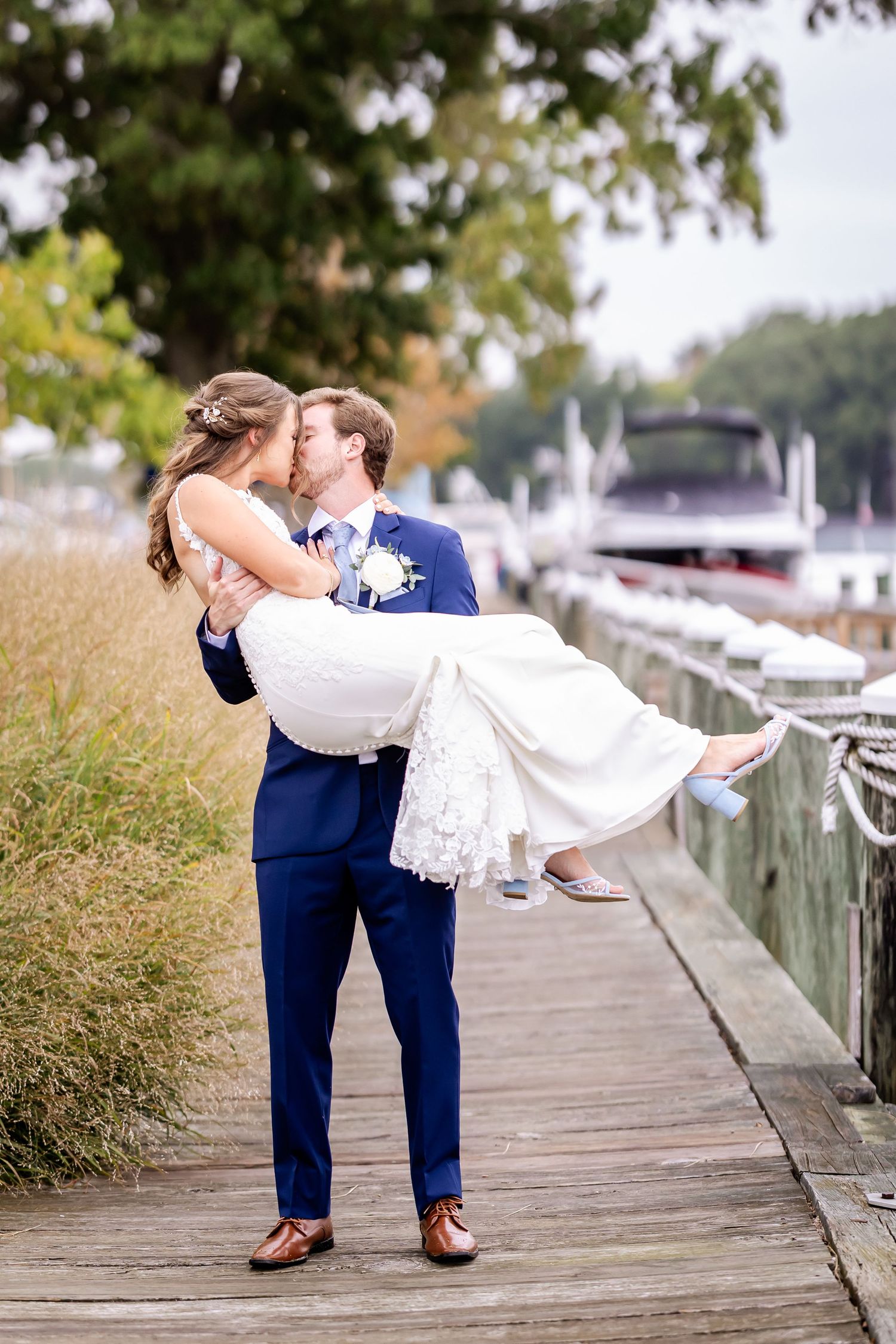 Romantic dip sequence of newlyweds on wooden dock with water and boats in background.