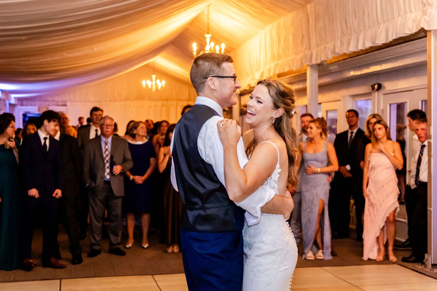A couple shares their first dance under warm lighting in an elegant tented reception space.