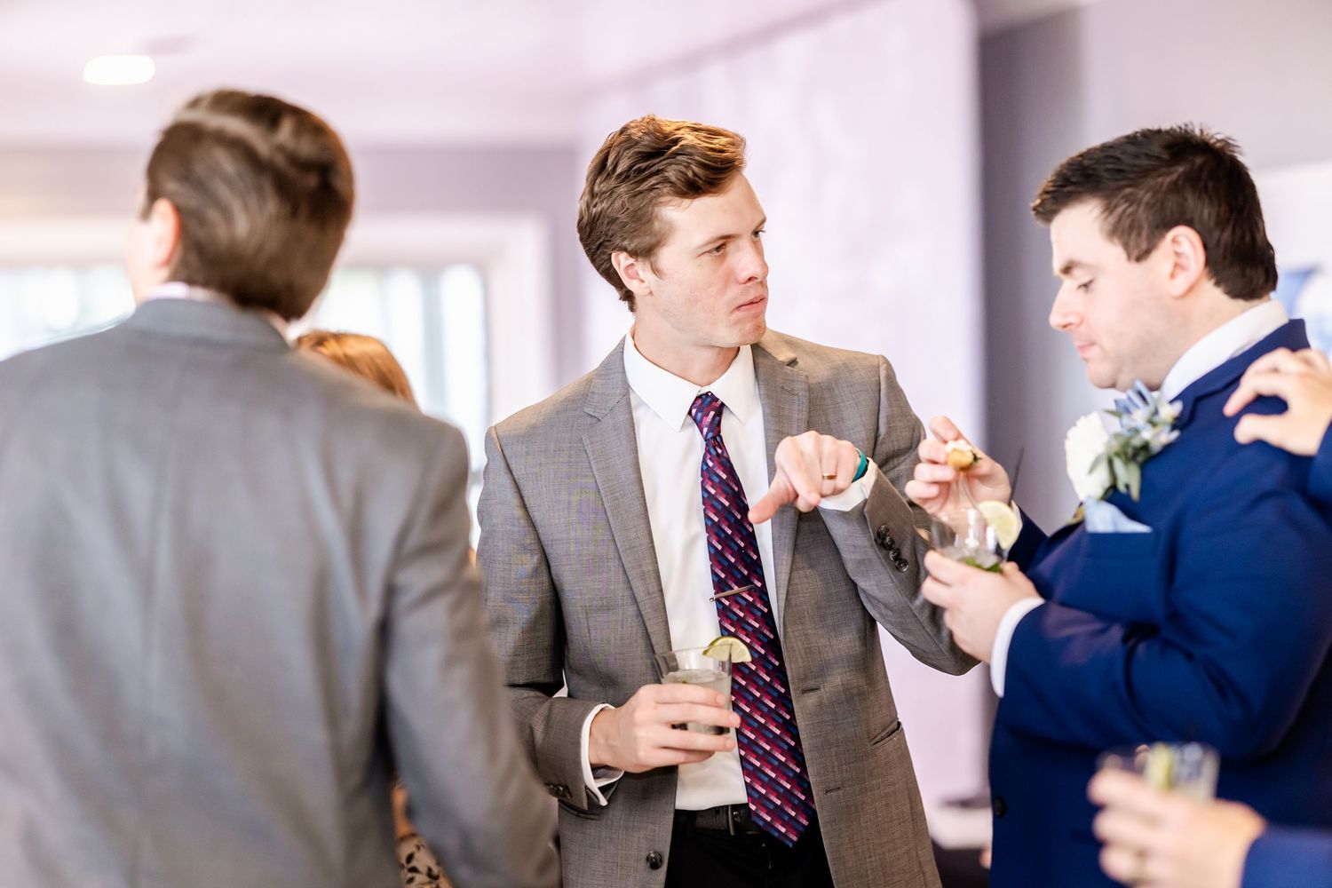 Wedding guests in formal attire socializing during an indoor reception.