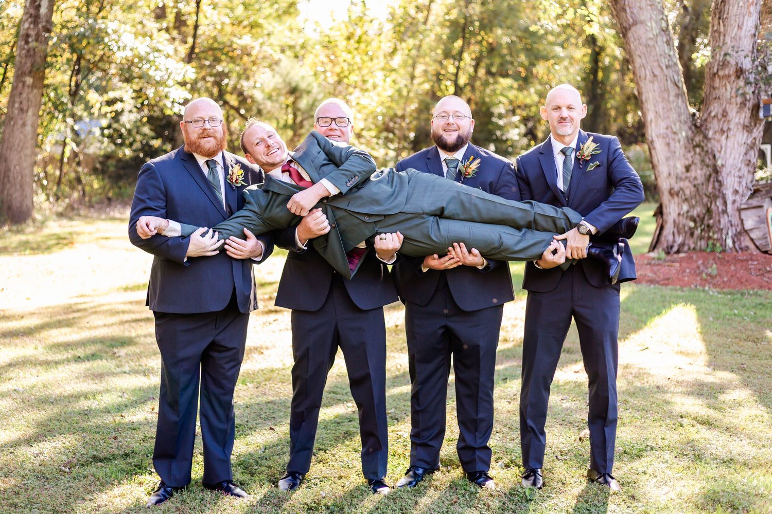 Groomsmen perform synchronized leg kicks for fun group photo outdoors.