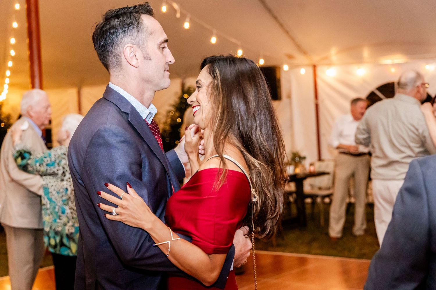 A couple shares an intimate dance moment under string lights at an evening wedding reception.