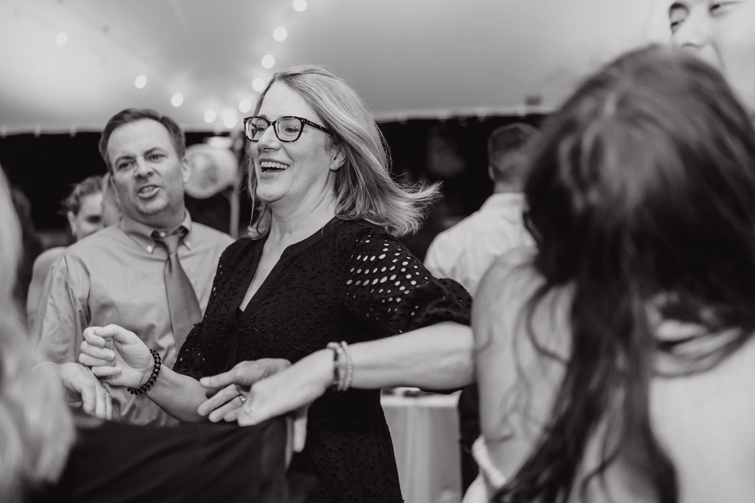 Wedding reception guests laugh and dance together on a dimly lit dance floor during celebration.