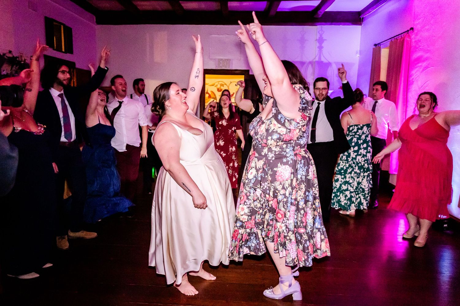 Wedding reception dancers celebrating with raised arms under purple mood lighting.