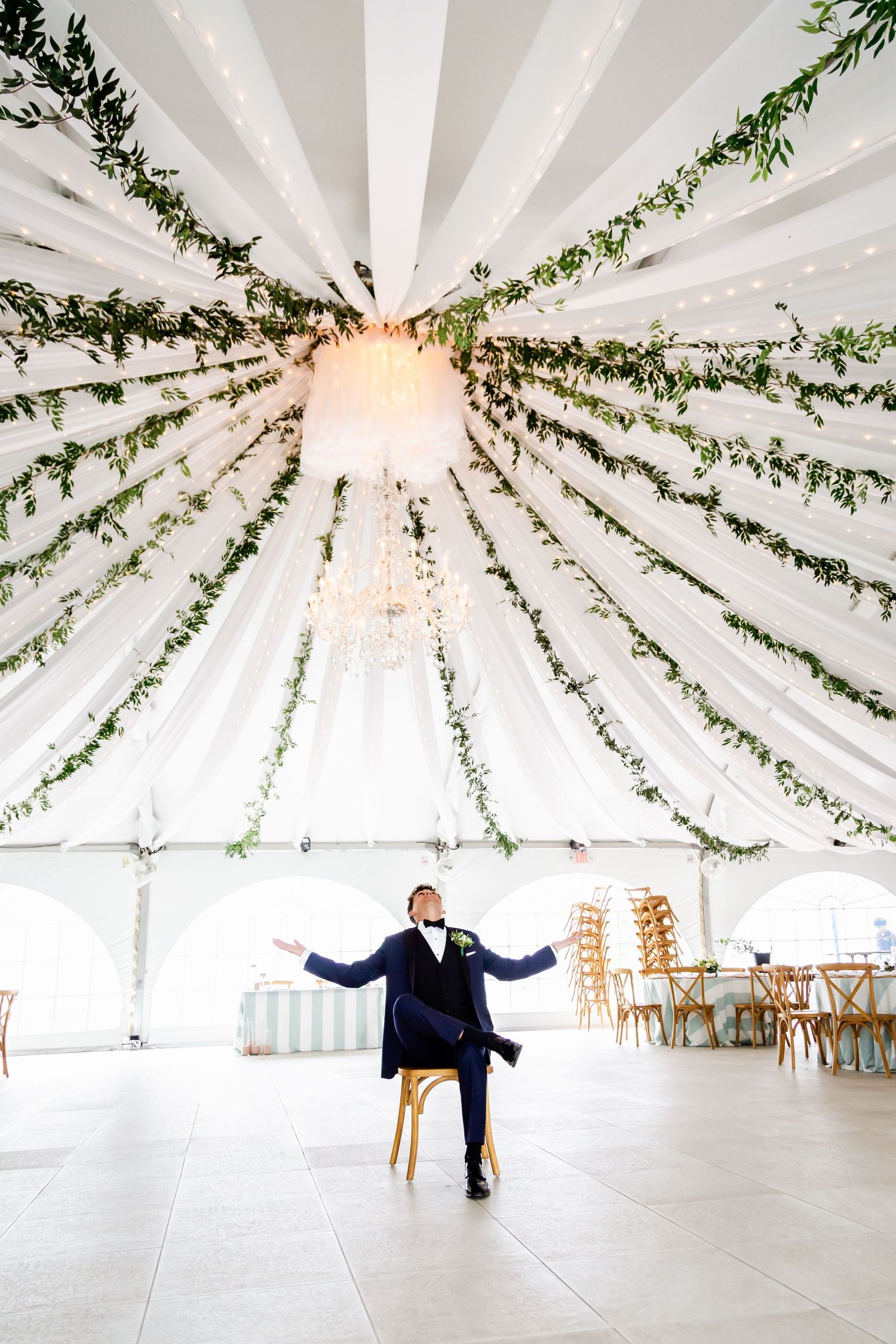 Elegant tent reception with white draping and greenery garlands creating a stunning sunburst ceiling design.