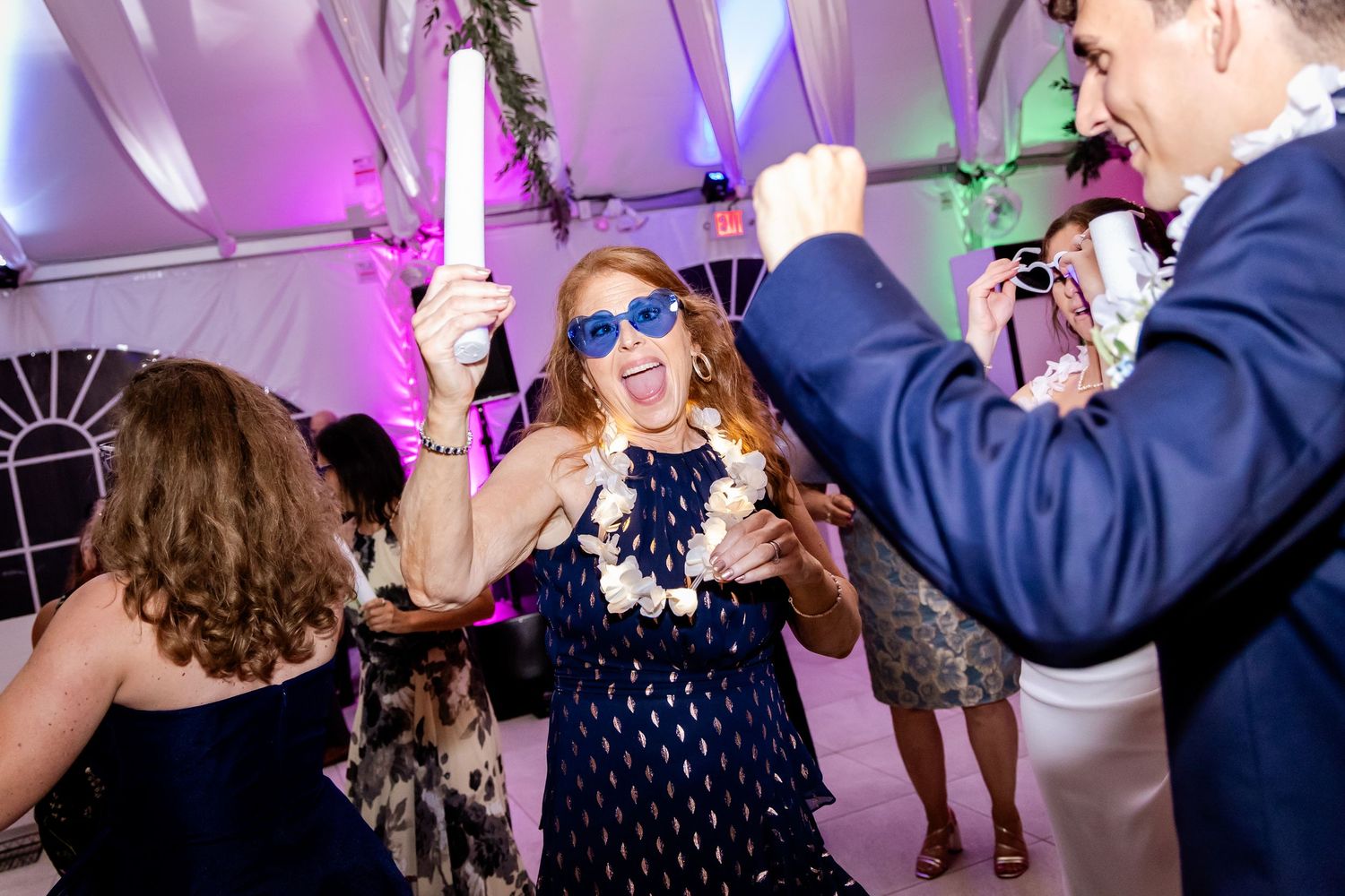 Wedding guests dancing and celebrating under a purple-lit tent at a reception.