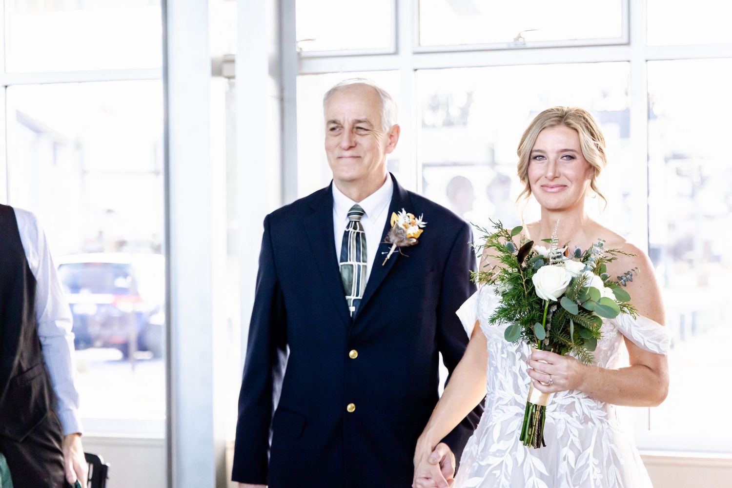 Wedding ceremony scene with bride holding white bouquet in bright indoor venue.