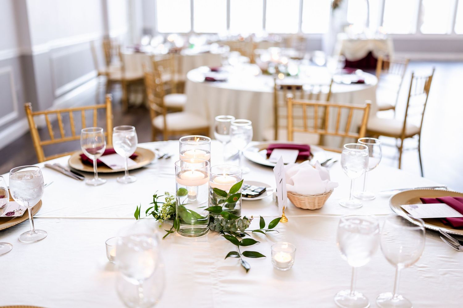 Elegant wedding reception table setting with white linens, gold chairs, and delicate greenery centerpieces.