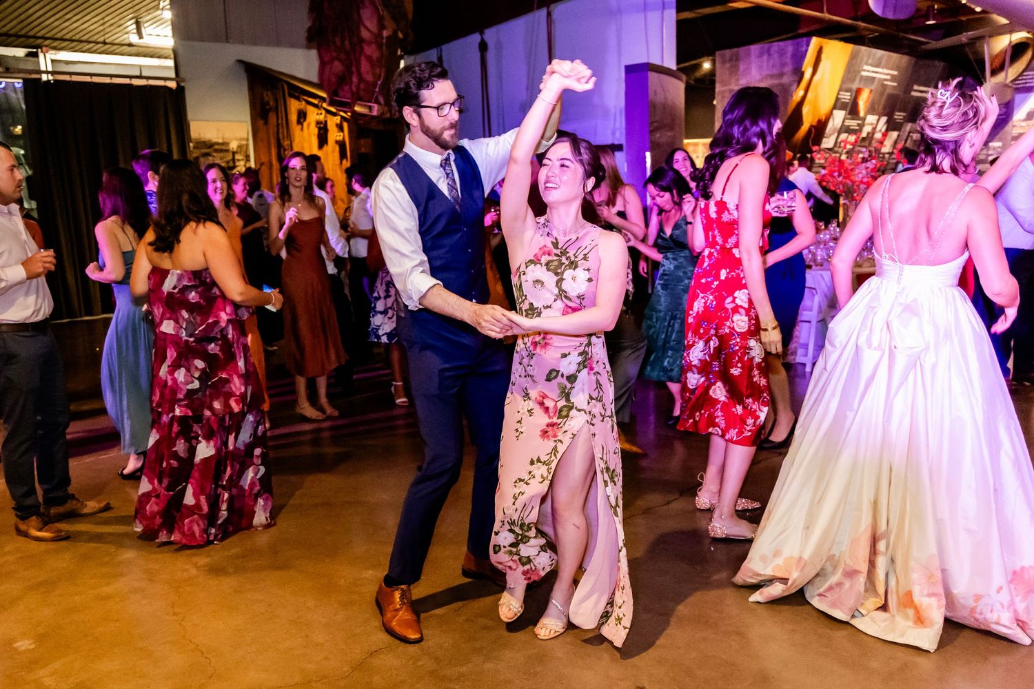 Lively wedding reception with couples dancing under colorful lighting.