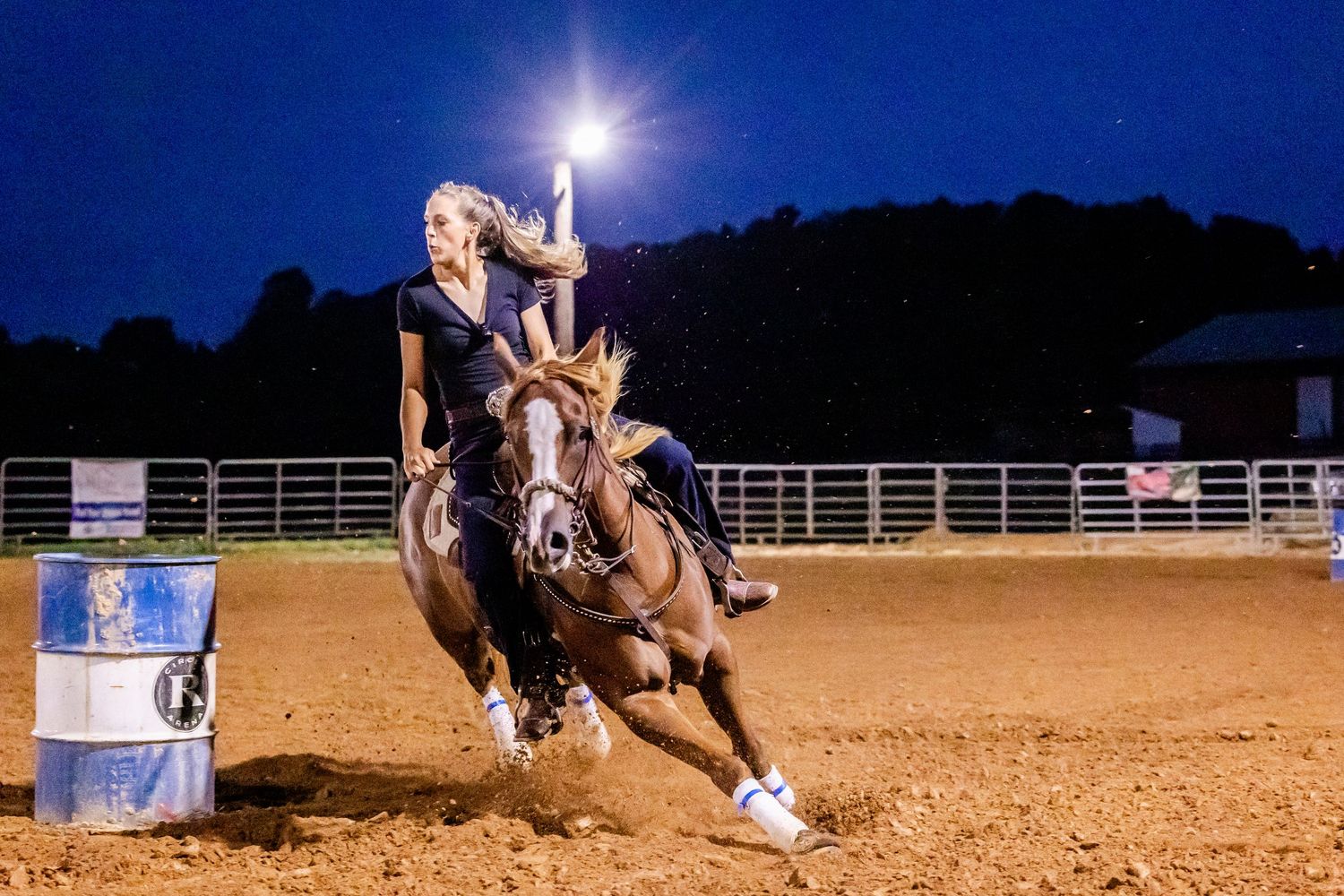 Horse and rider competing in barrel racing at night under arena lights.