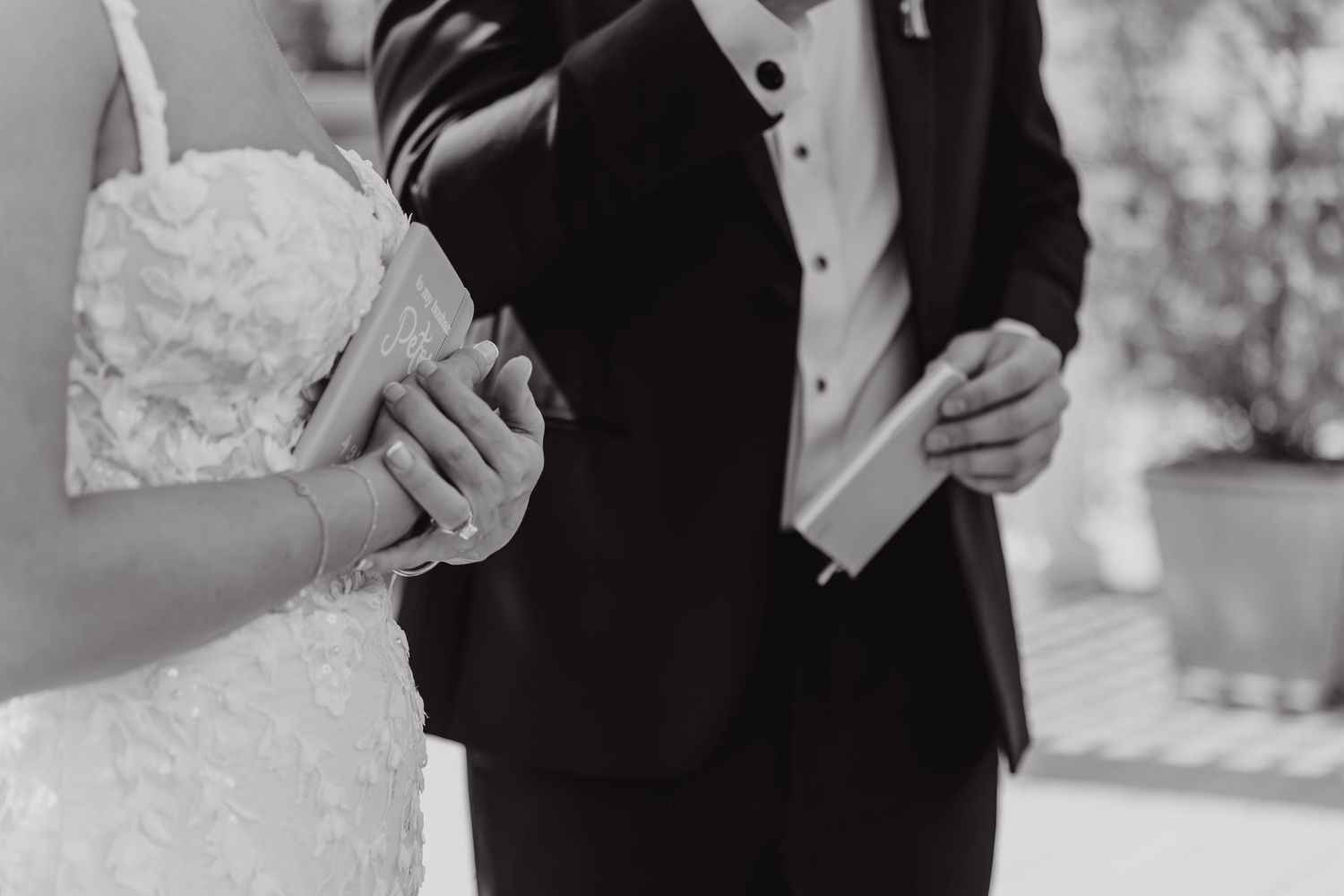 Black and white close-up of formal wedding attire and hands during a ceremony.
