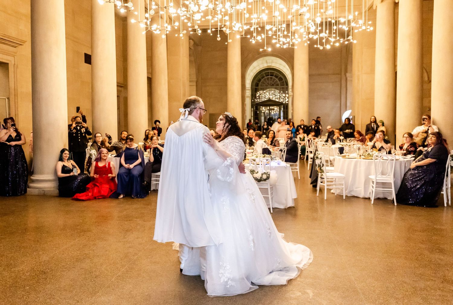 A romantic first dance under crystal chandeliers in an elegant ballroom with classical columns.