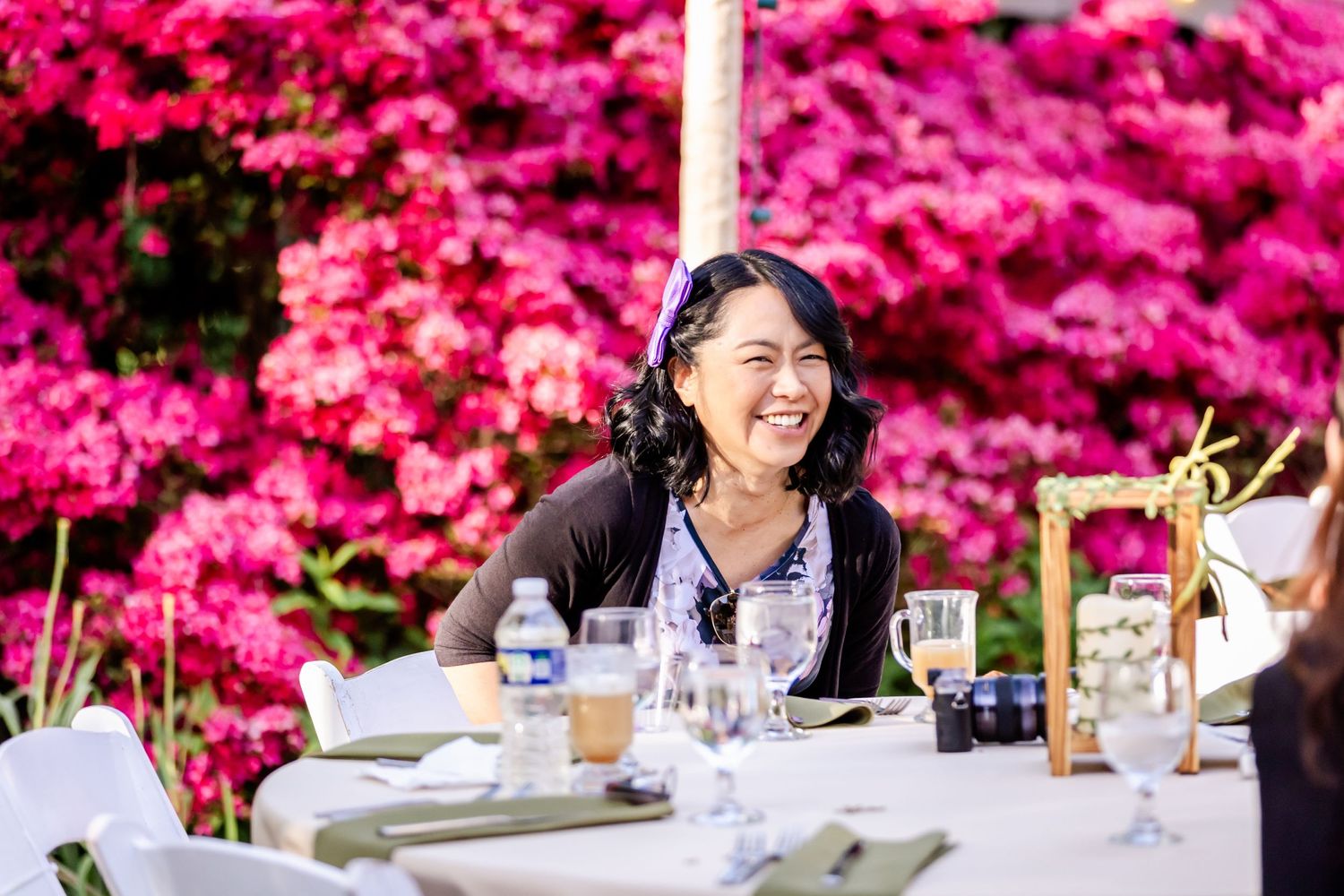 Outdoor dining table set against vibrant pink azalea bushes in full bloom.