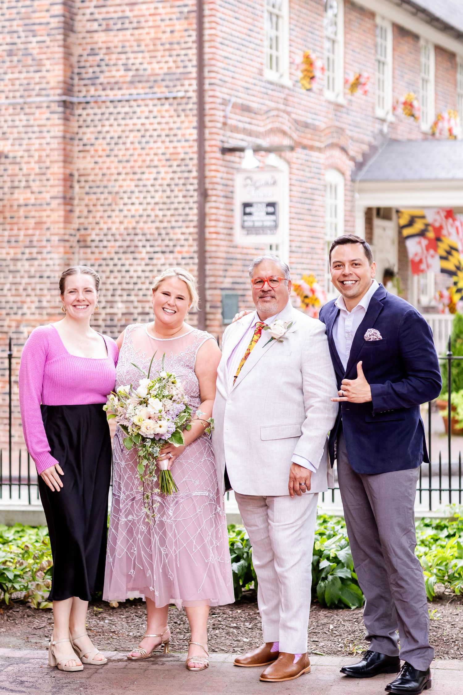 Wedding party members pose outside historic brick building with decorative flags.