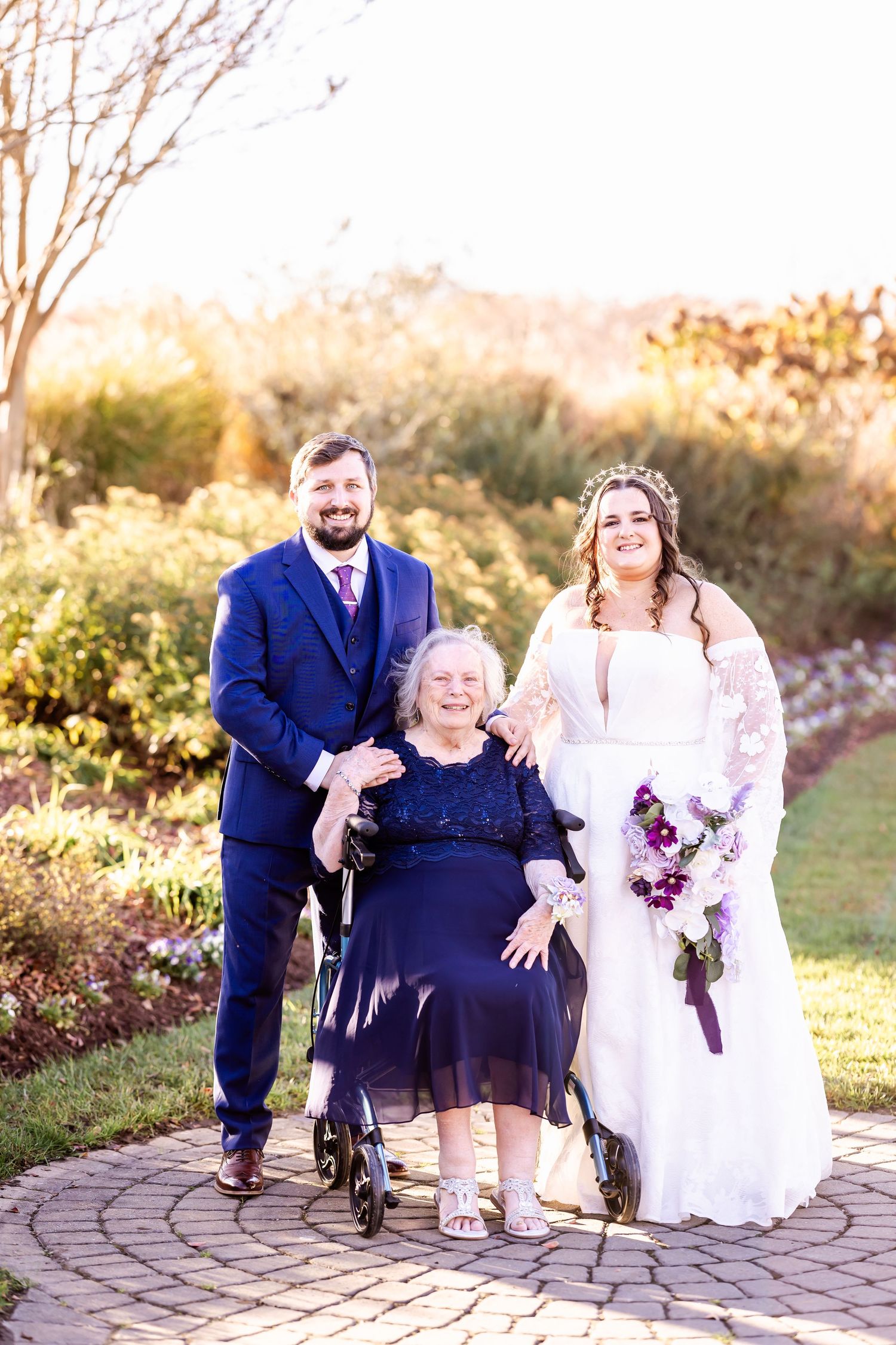 Heartwarming wedding photo with couple and guest in wheelchair on stone pathway.