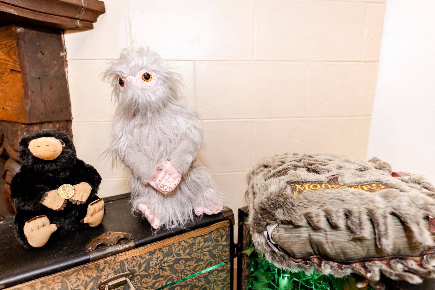 White plush creature and black stuffed animal displayed on fireplace mantle.