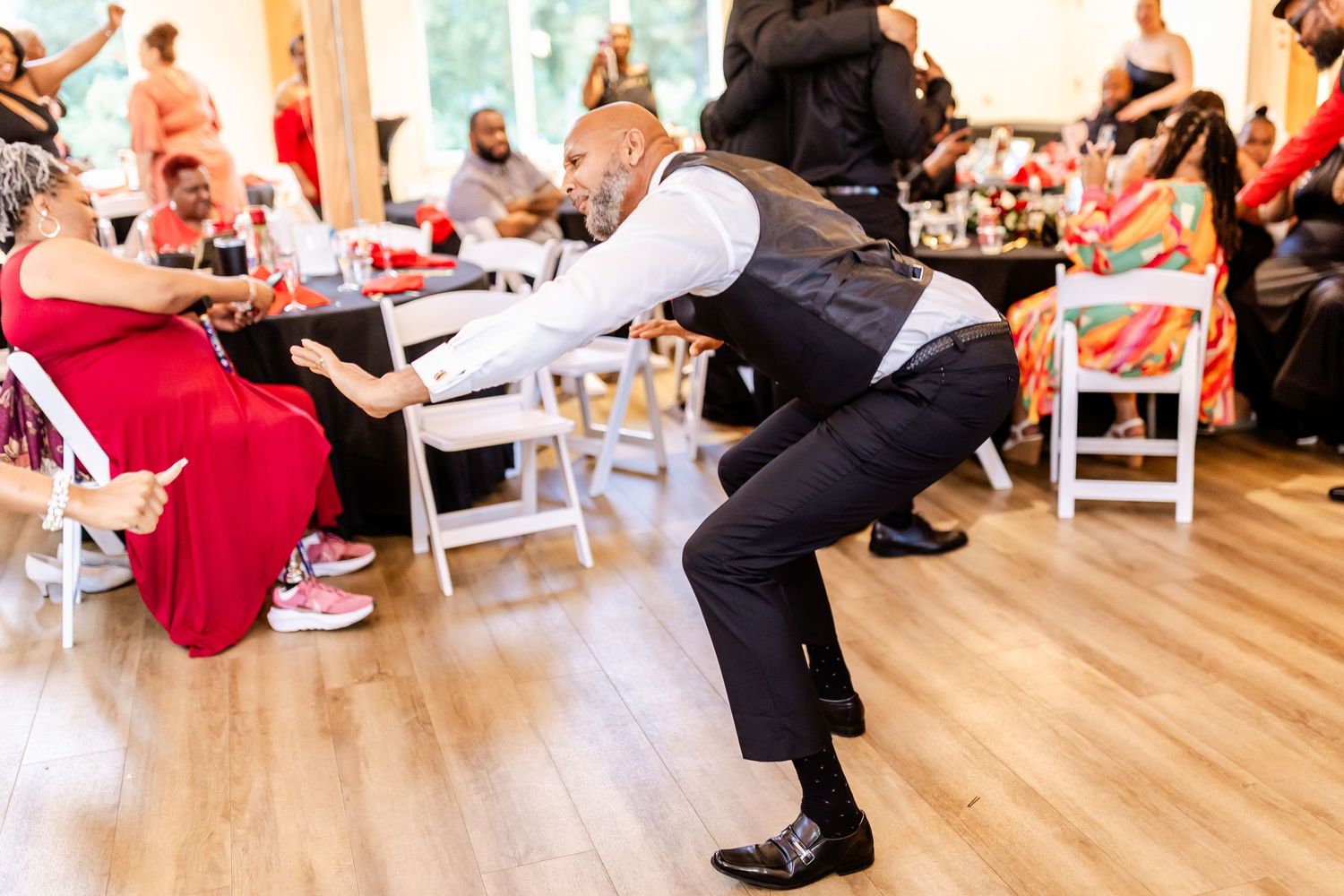 Wedding guest performs energetic dance move on hardwood floor during reception.