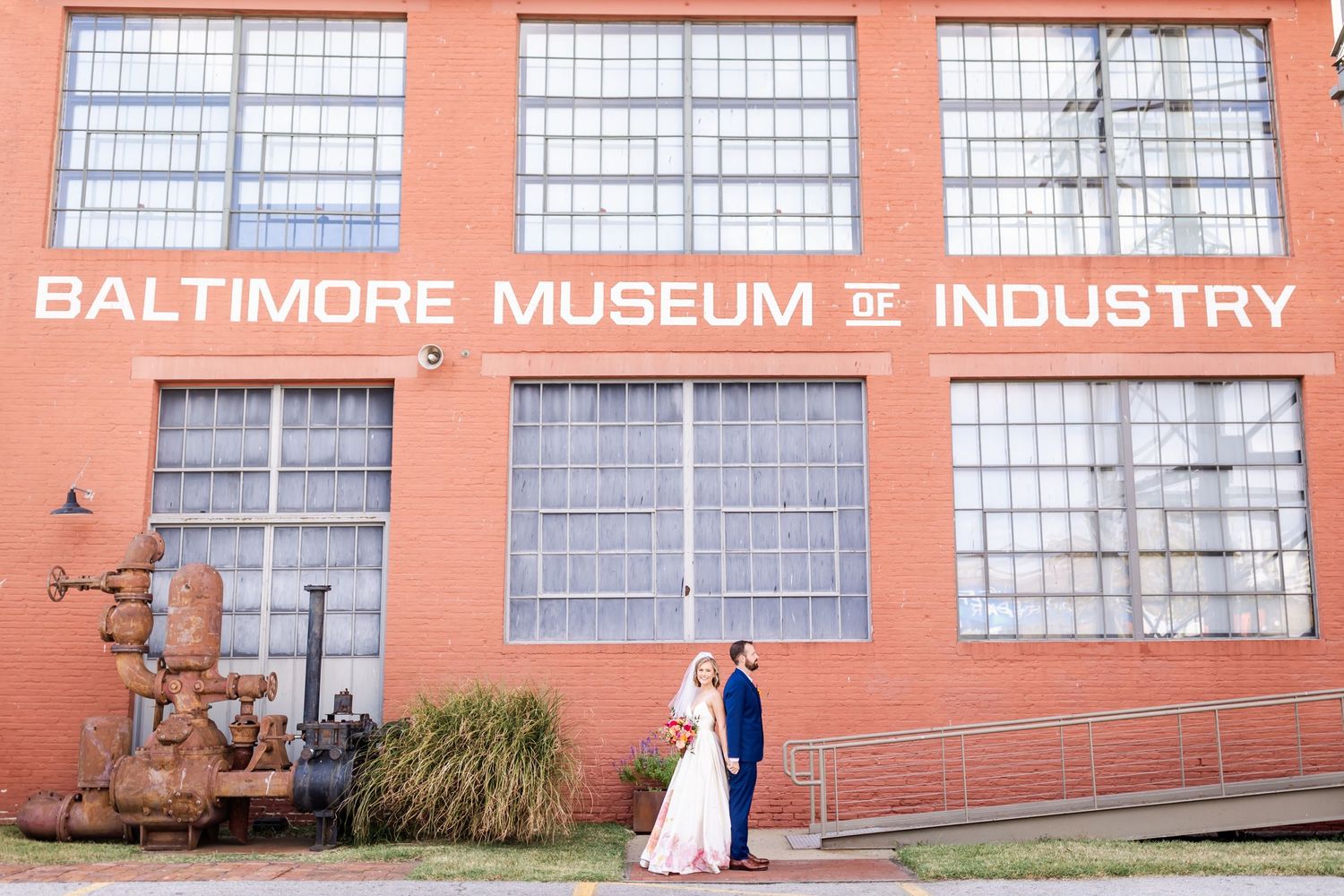 Wedding couple poses outside the Baltimore Museum of Industry's brick facade.