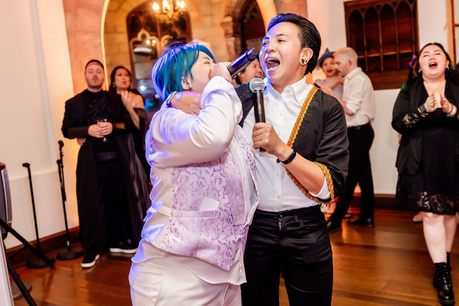 Party guests performing an energetic karaoke duet in formal attire at an indoor venue.