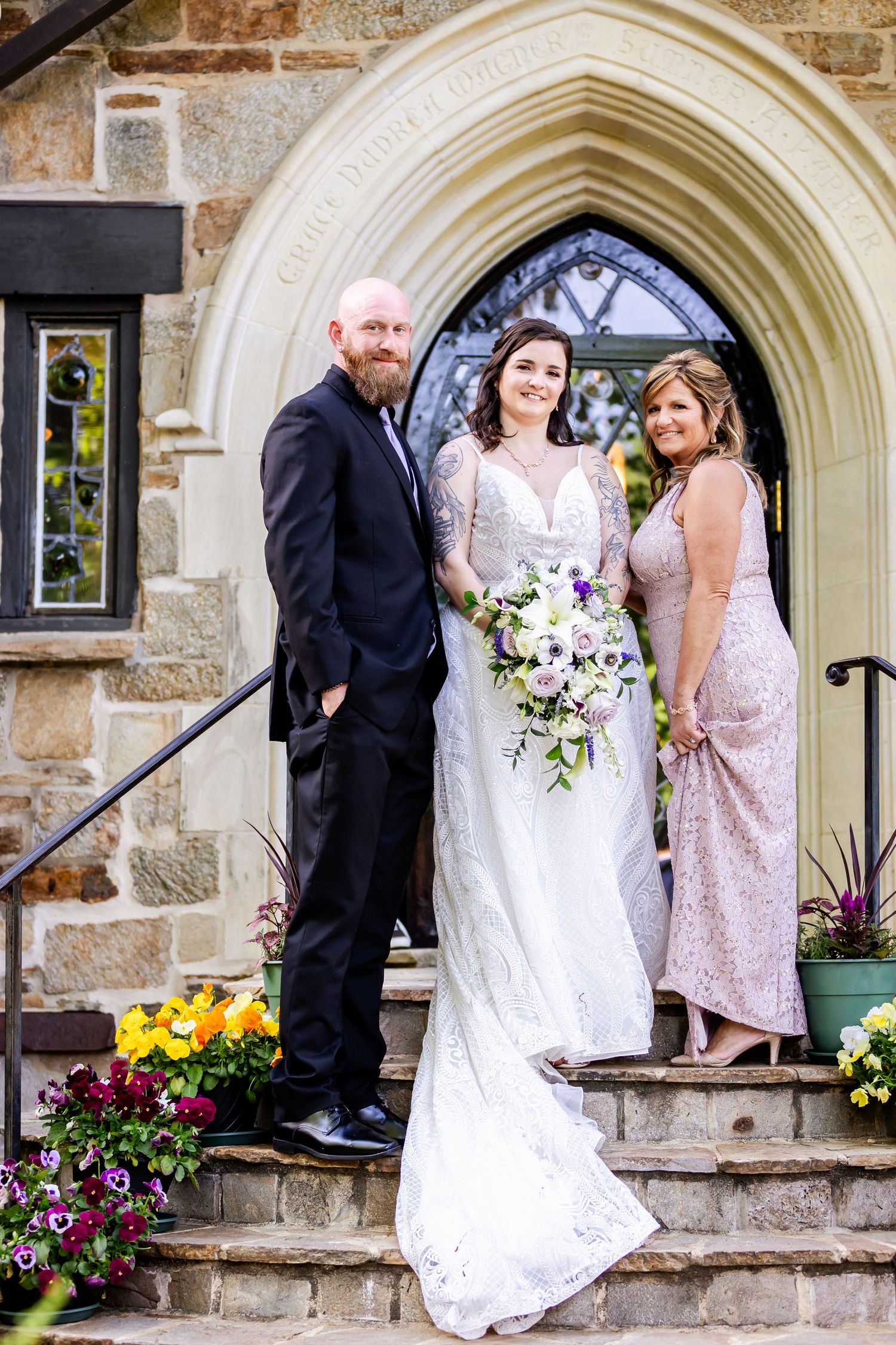 Wedding portrait on church steps with stone archway and decorative spring flowers.